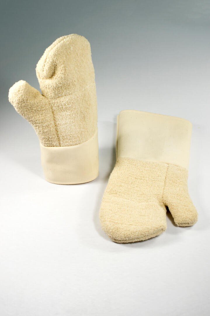 Zwei beigefarbene Ofenhandschuhe mit strukturiertem Stoff und glatten Bündchen, von denen einer aufrecht steht und der andere flach auf einer weißen Fläche mit hellgrauem Hintergrund liegt.