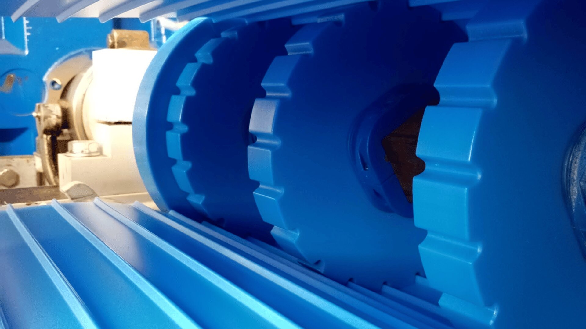 Close-up view of interlocking blue industrial gears or rollers, showing their detailed ridged and grooved surfaces as part of a larger mechanical machine.
