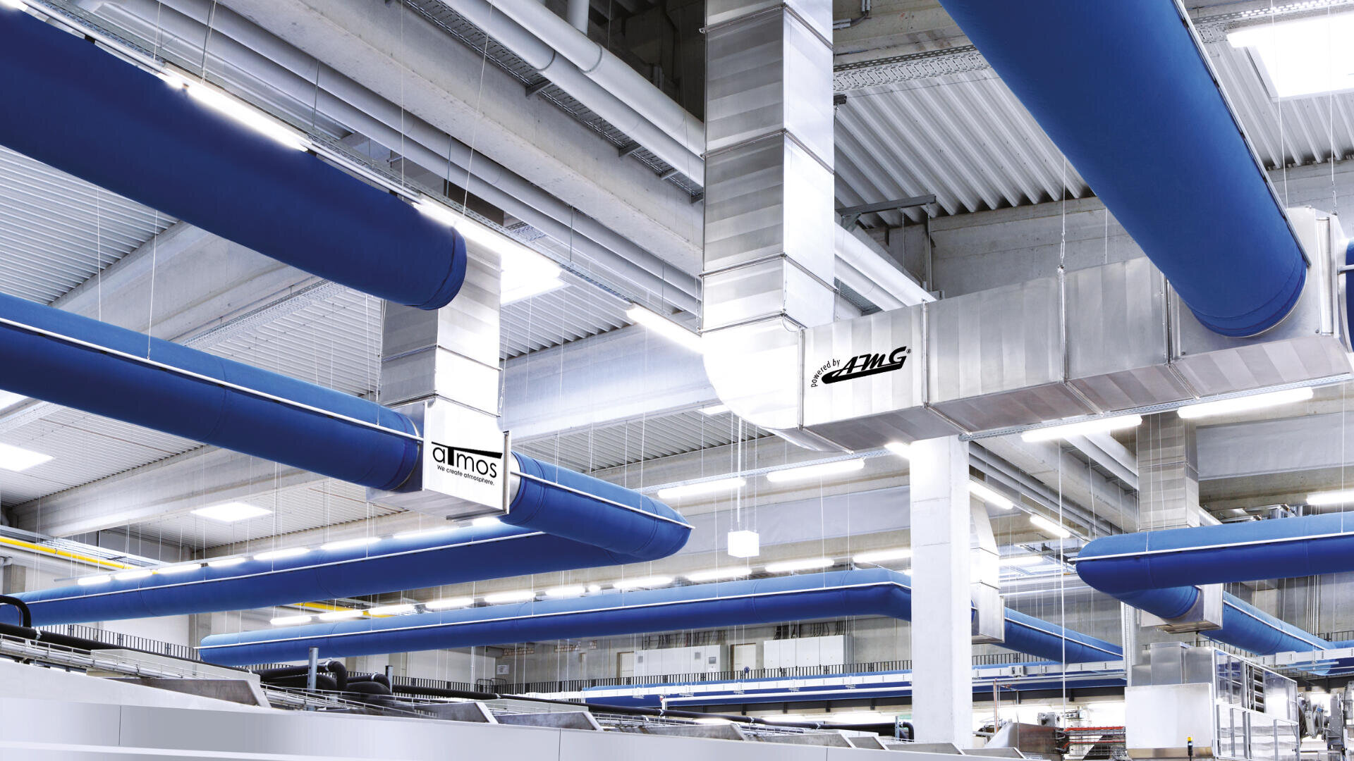 Industrieller Innenraum mit freiliegenden Luftkanälen aus blauem Stoff und einem von der Decke hängenden silbernen Metalllüftungssystem, das von einer hellen Deckenbeleuchtung beleuchtet wird. An den Kanälen sind Schilder mit der Aufschrift almos und DLHG zu sehen.