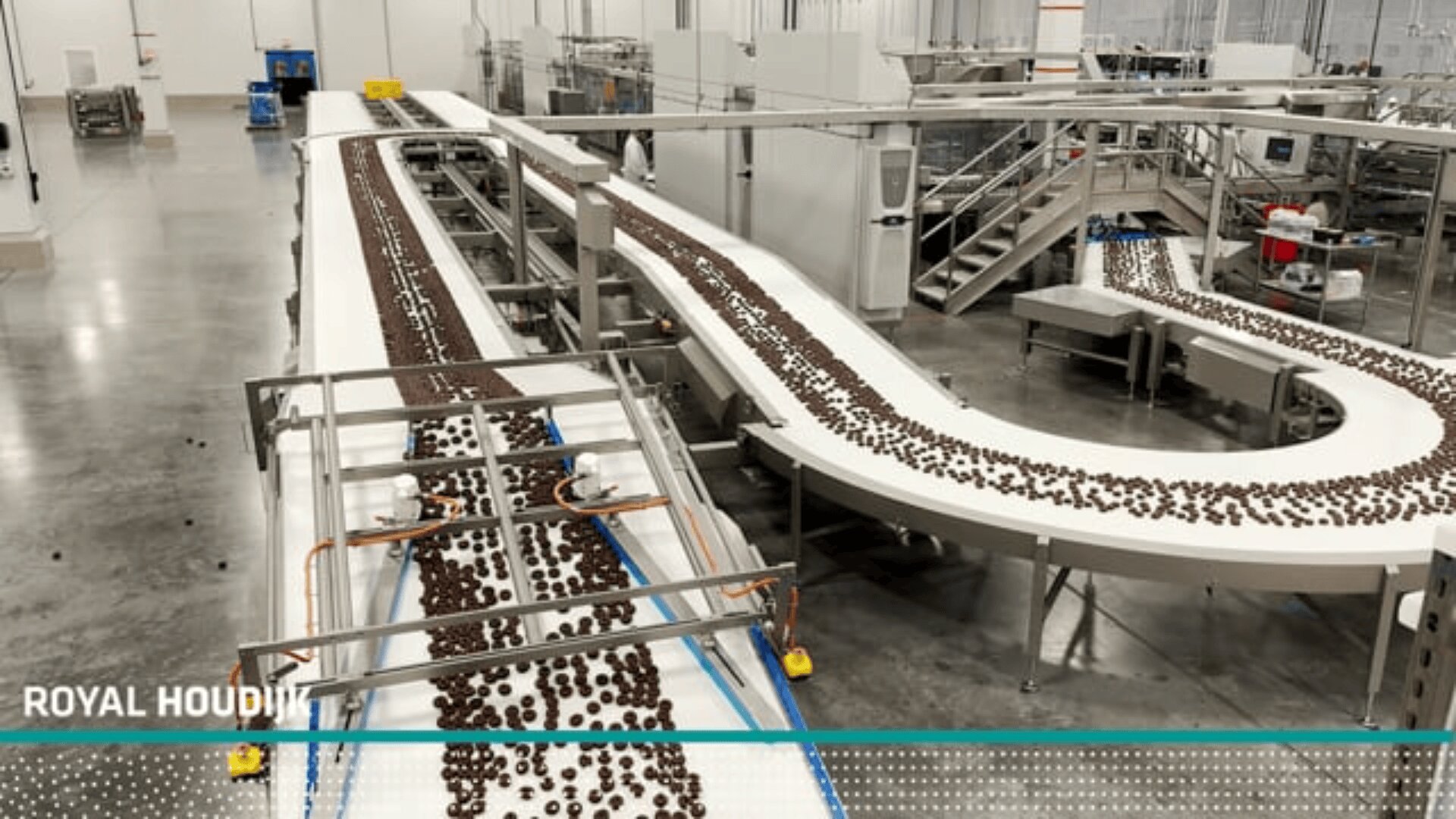 A factory production line with conveyor belts transporting rows of chocolate cookies through a large, clean industrial facility.