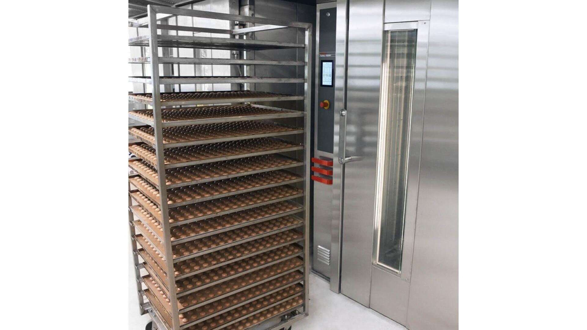 A metal rack filled with trays of eggs stands next to a large stainless steel industrial incubator or oven in a clean, modern facility.
