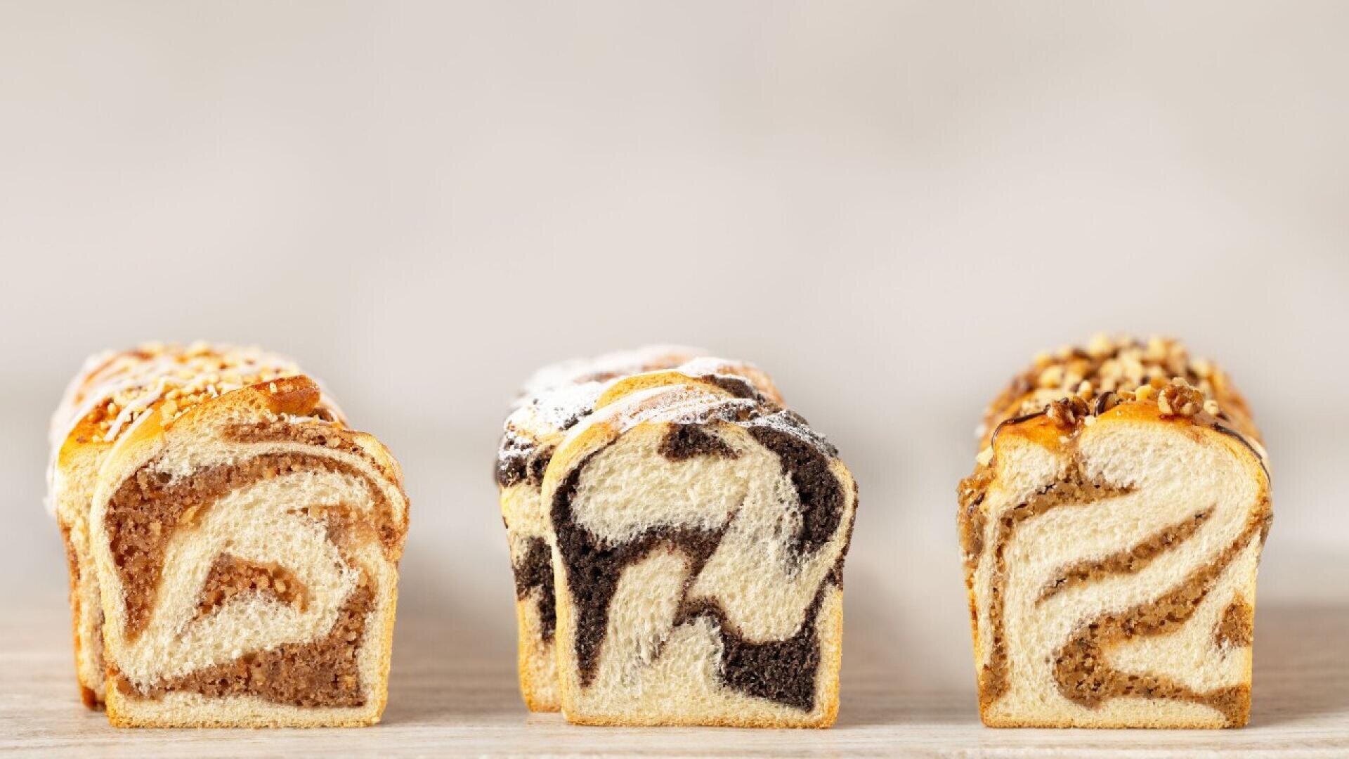 Three slices of marble bread with different fillings are arranged side by side on a light wooden surface, each showing a distinct swirl pattern and different toppings.