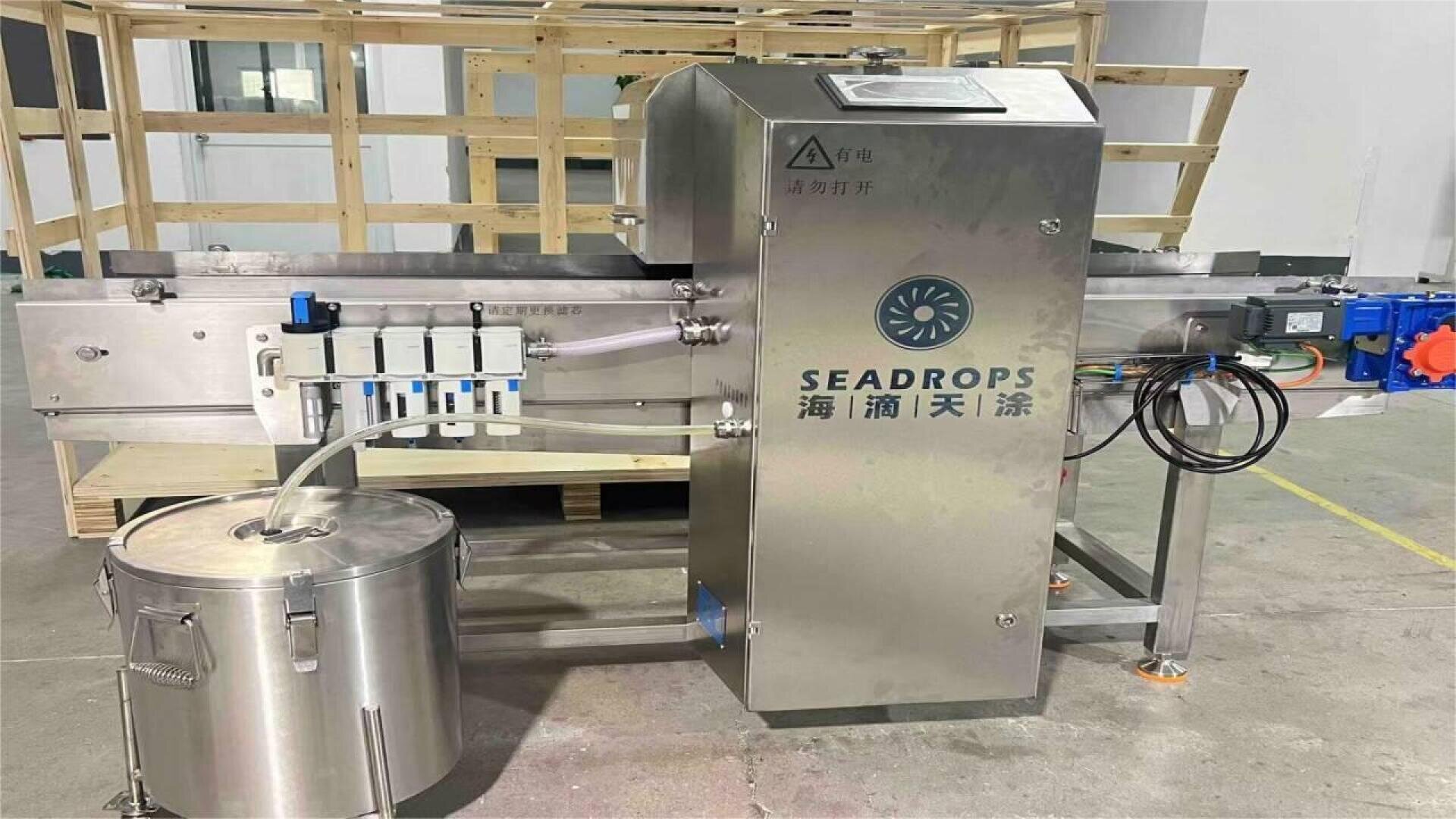 A stainless steel industrial machine labeled “SEADROPS” with Chinese text stands indoors next to a large metal container and wooden crates in the background. Cables, pipes, and control components are visible on the unit.