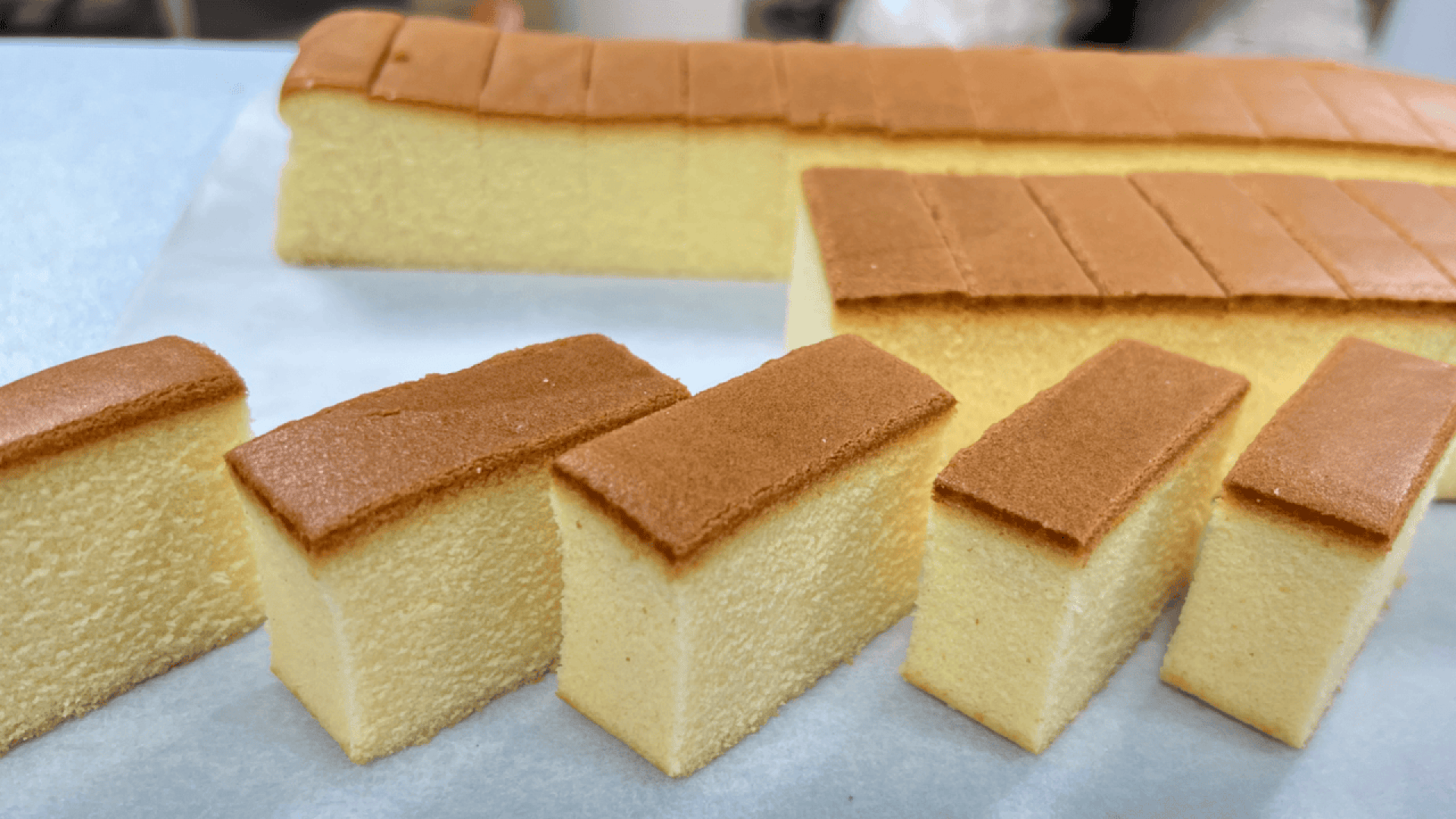 Rechteckige Scheiben aus flauschigem, goldbraunem Biskuit sind auf einer weißen Oberfläche fein säuberlich angeordnet und zeigen ihre weiche Textur und gleichmäßige, glatte Oberseite.