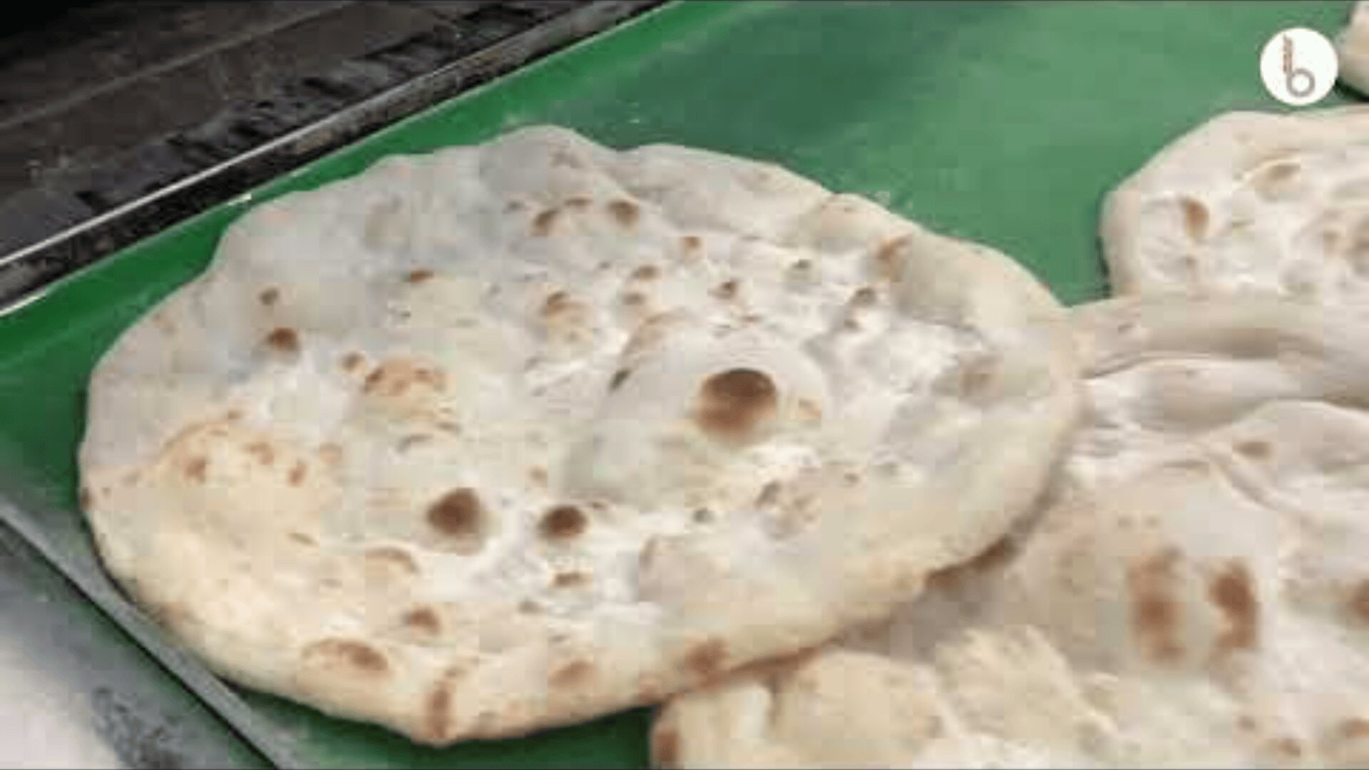 Round pieces of flatbread with brown spots are placed on a green surface, likely cooling after being freshly baked.