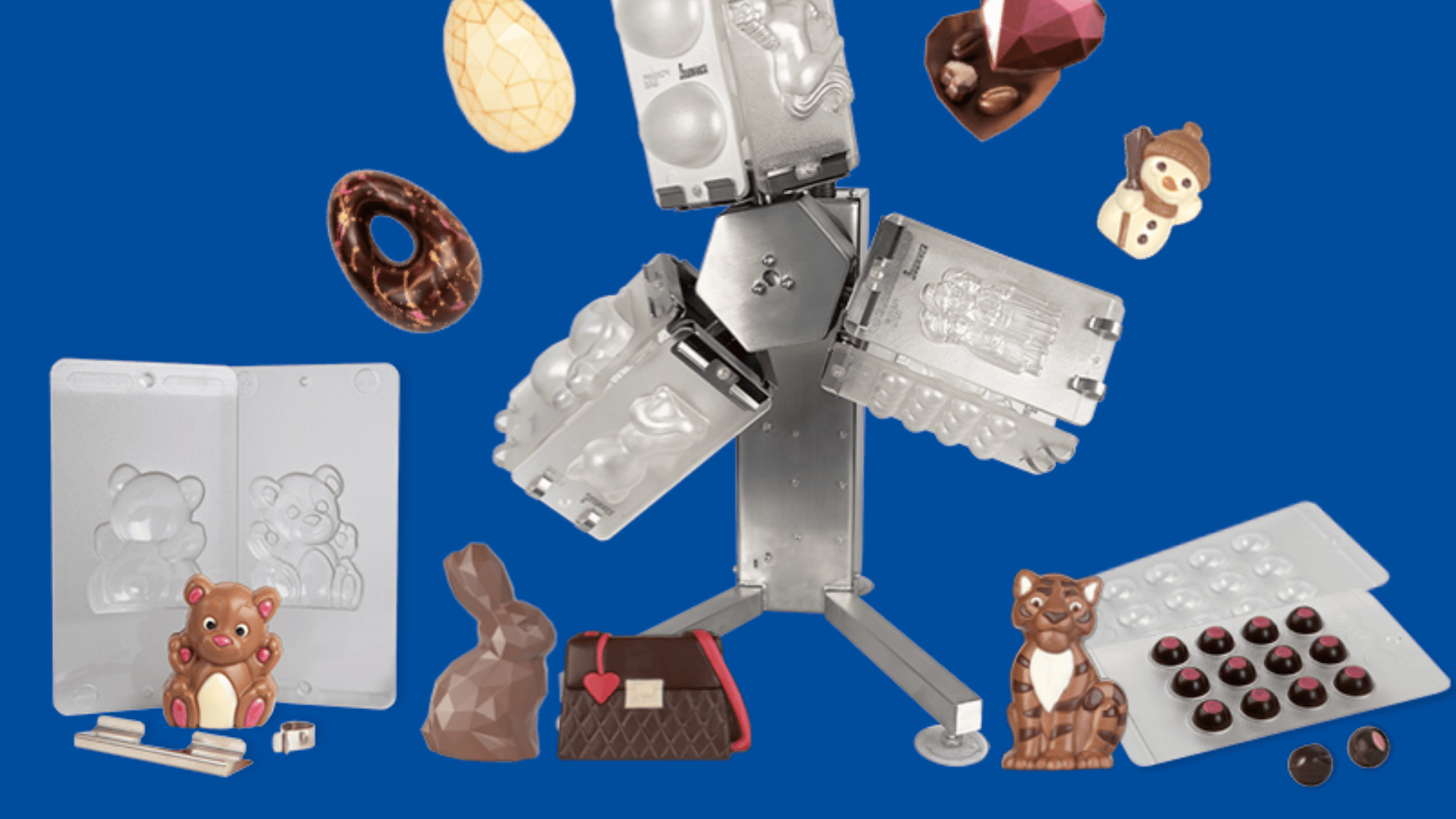 A variety of chocolate molds, including bear, bunny, egg, and heart shapes, surround a metal rotary molding machine, all set against a solid blue background.