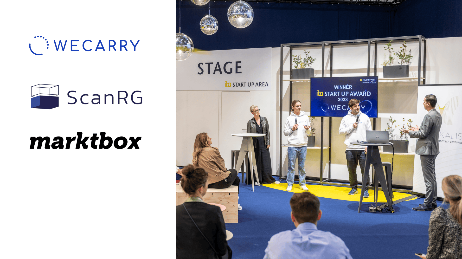 Menschen beobachten vier Personen auf der Bühne eines Startup-Events. Hinter ihnen steht ein Schild mit der Aufschrift „WINNER IN START UP AWARD 2023“. Links sind die Logos von WECARRY, ScanRG und marktbox zu sehen.