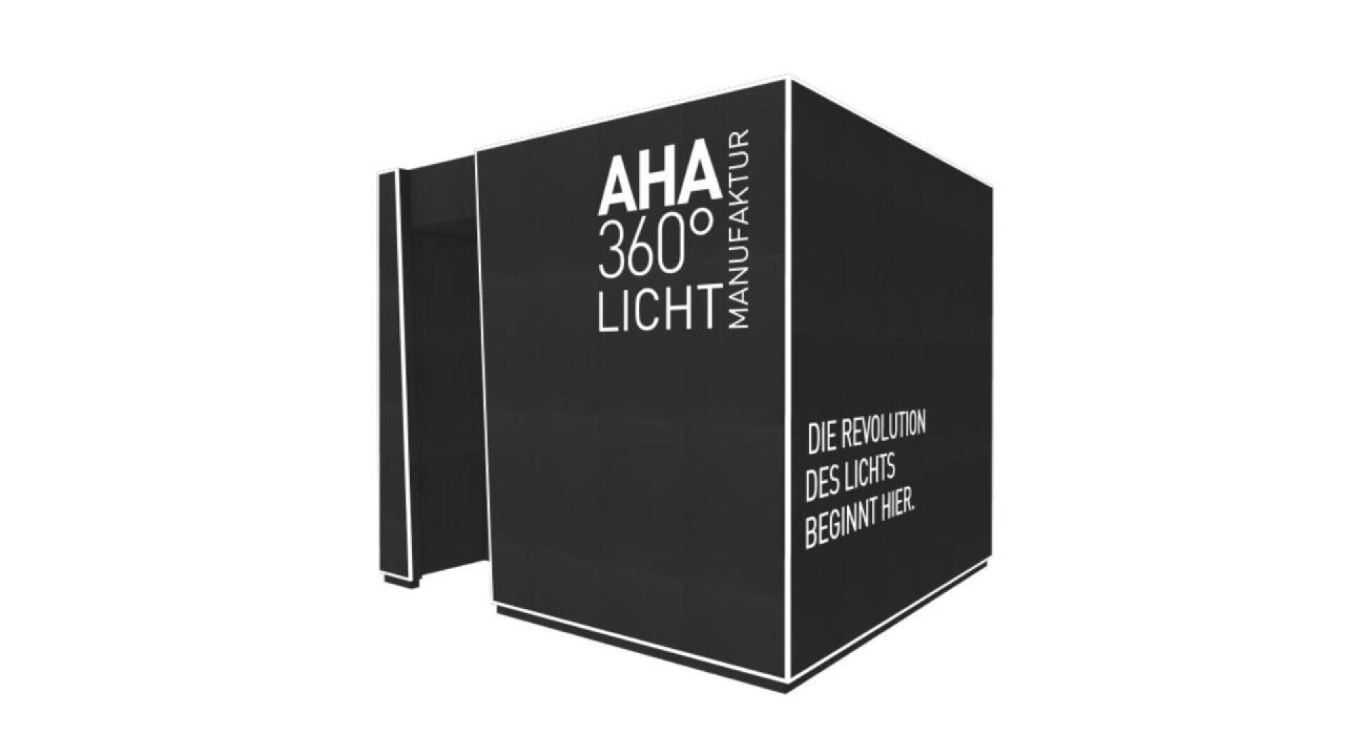 A large black cube-shaped structure with white text reading AHA 360° LICHT MANUFAKTUR and DIE REVOLUTION DES LICHTS BEGINNT HIER on its sides, set against a plain white background.