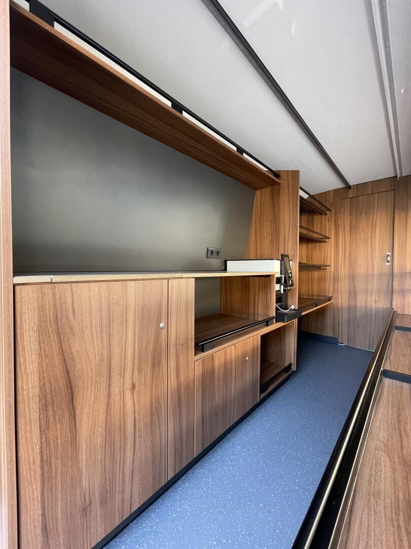 Modernes Interieur mit holzgetäfelten Schränken und Regalen, einem eingebauten Arbeitsbereich, blau gesprenkeltem Fußboden und grauen Wänden, die ein schlichtes, minimalistisches und funktionales Design ergeben.