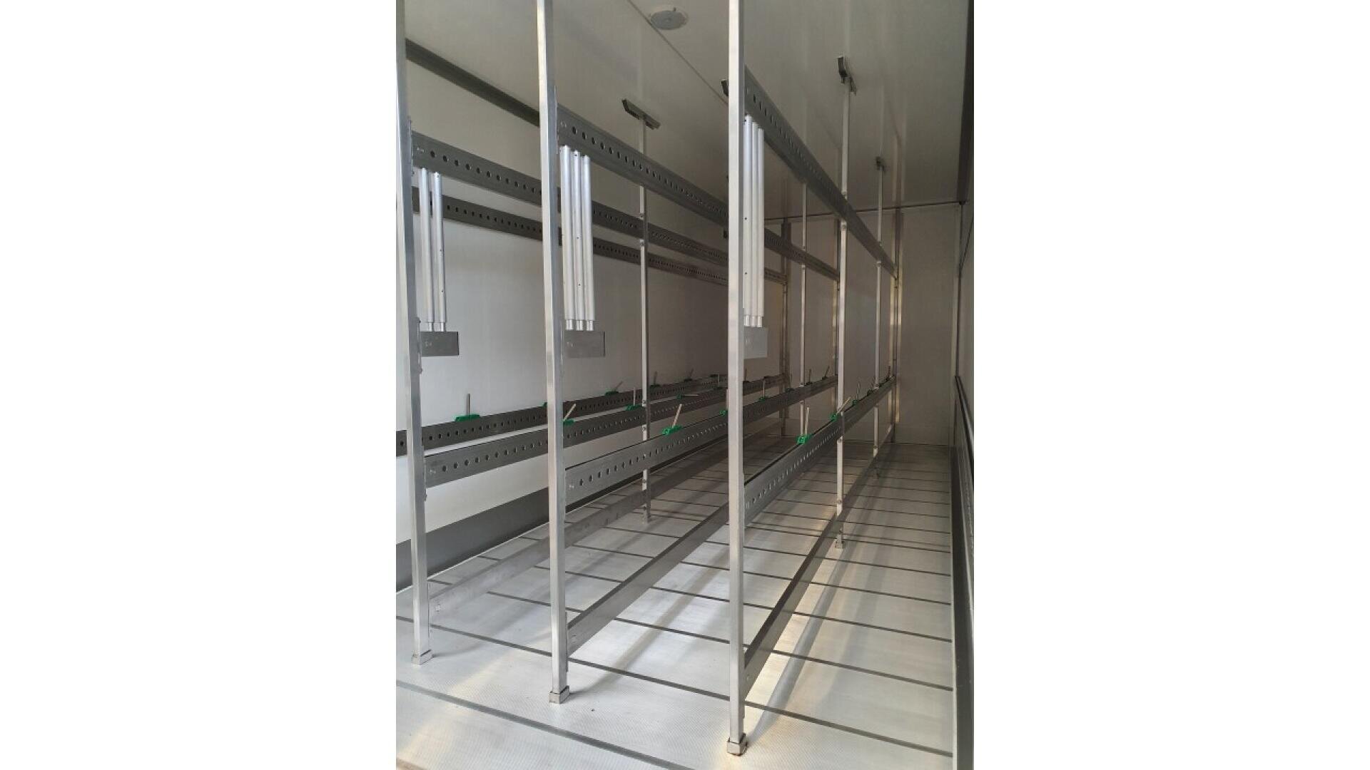 Interior view of an empty refrigerated truck, featuring stainless steel hanging rails and support bars along the ceiling and walls, with a clean, metallic floor and bright lighting.
