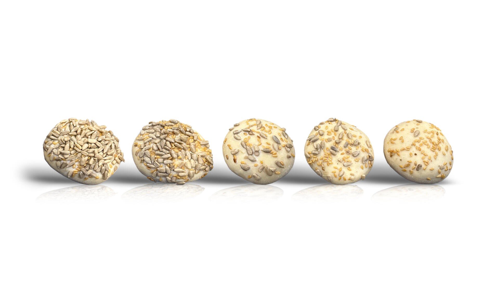 Five round bread rolls in a row, each topped with different seeds such as sunflower seeds and possibly sesame or cheese, on a white background with a subtle reflection underneath.