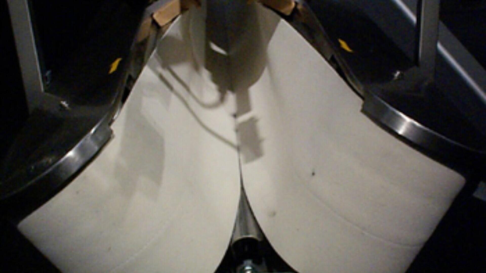 Close-up view of two large white rolls of toilet paper held in a metal dispenser, with a shadow cast between them and part of the dispenser mechanism visible at the bottom.