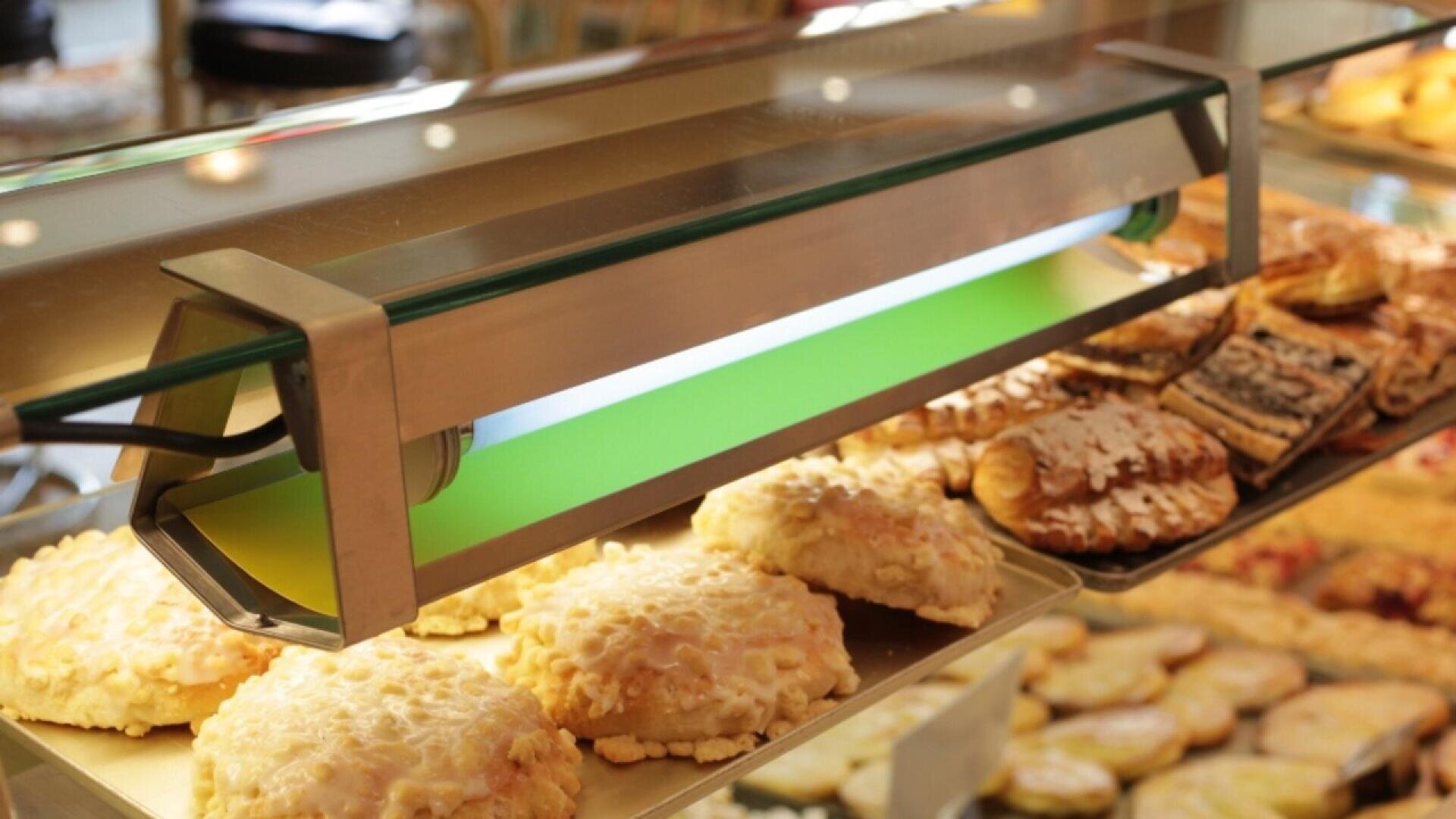 A close-up of assorted pastries displayed on trays under a green insect zapper in a bakery or café setting. The pastries are topped with icing and appear freshly baked.