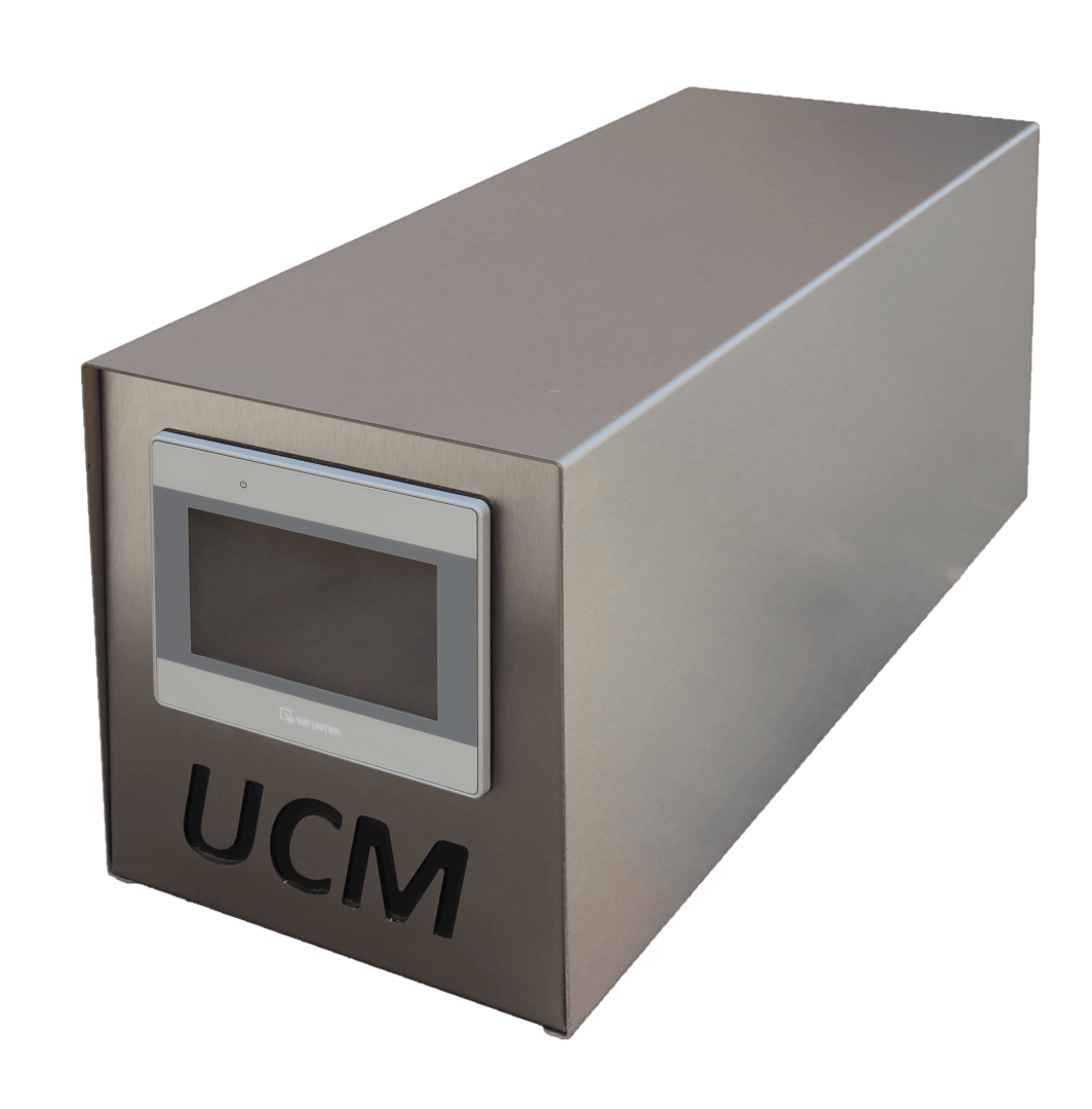 A rectangular metallic device with a digital screen on the front and the letters UCM cut out below the screen. The device sits on a plain surface with a white background.