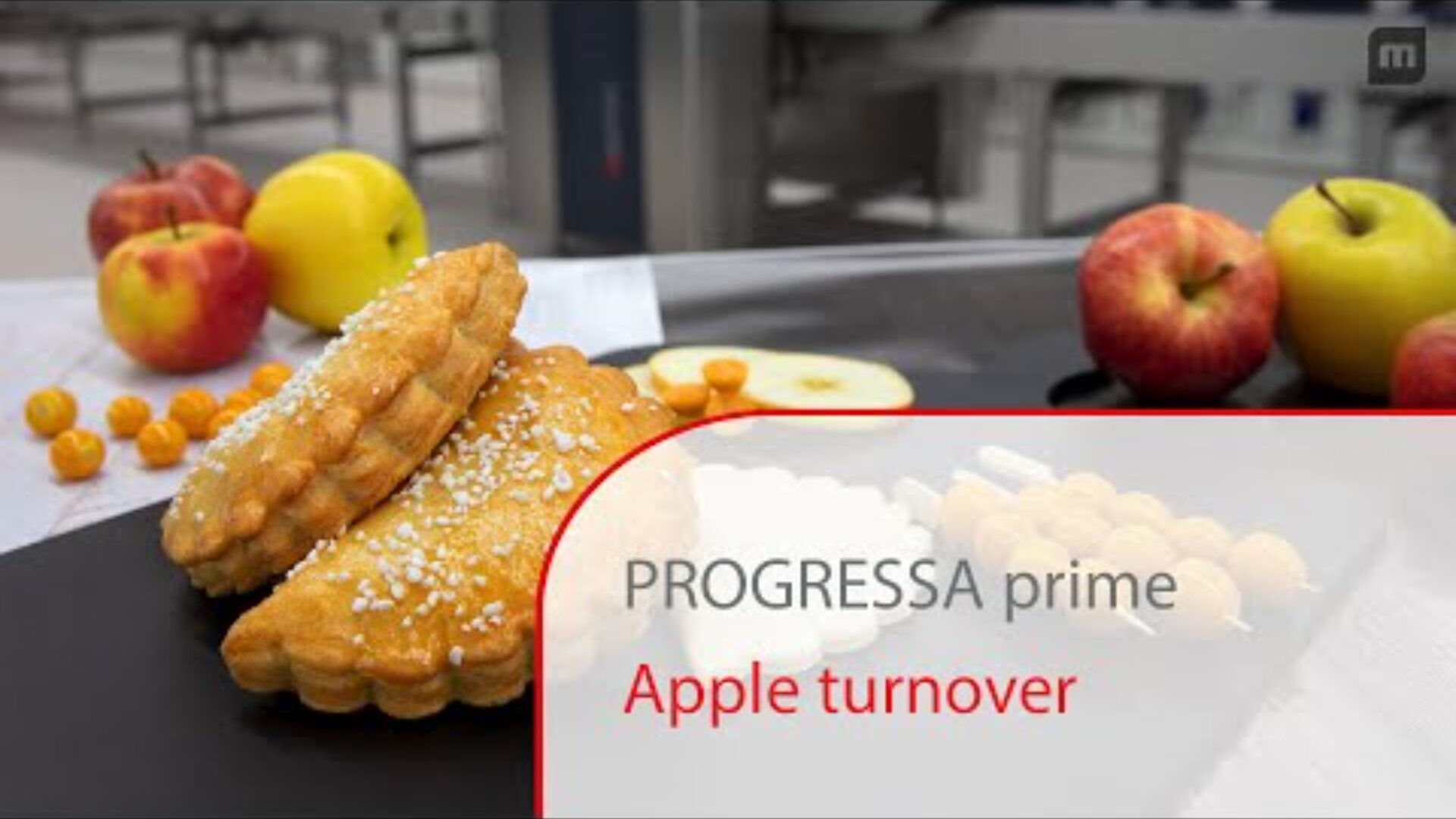 Zwei mit Zucker bestreute Apfeltaschen liegen auf einem schwarzen Tablett, umgeben von frischen Äpfeln und Apfelscheiben. Ein unscharfer Hintergrund zeigt eine moderne Küche oder Bäckerei. Der Text auf dem Bild lautet: PROGRESSA prime Apple turnover.