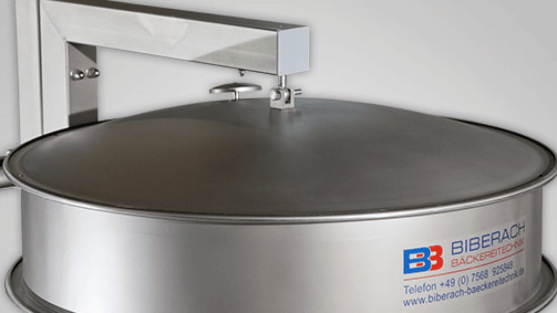 Eine Nahaufnahme einer großen Industriemaschine aus Edelstahl mit gewölbtem Deckel, an deren Seite sich das Logo und die Kontaktinformationen der Biberach Bäckereitechnik befinden.