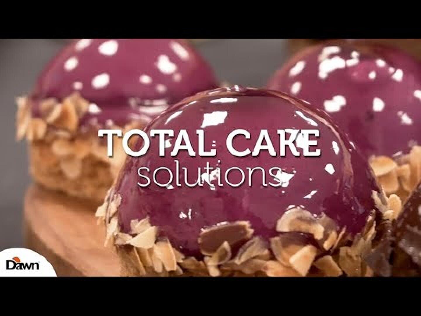 Glossy purple dome cakes with a shiny finish and almond slices at the base, with the text TOTAL CAKE solutions overlaid. Dawn logo appears in the bottom left corner.