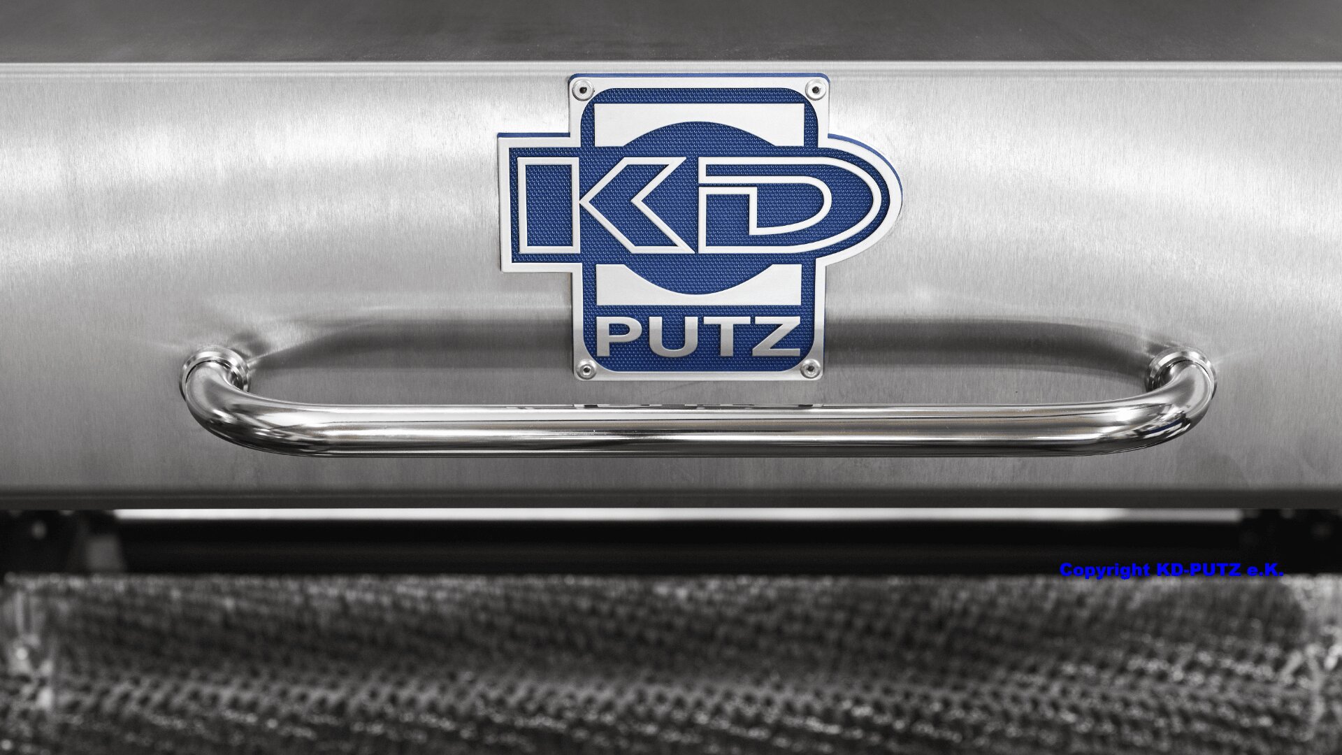 Nahaufnahme einer metallischen Oberfläche mit einem Chromgriff und einer blau-weißen KD PUTZ-Logoplatte in der Mitte. Unten sind reflektierende Texturen und ein Netzmaterial sichtbar.