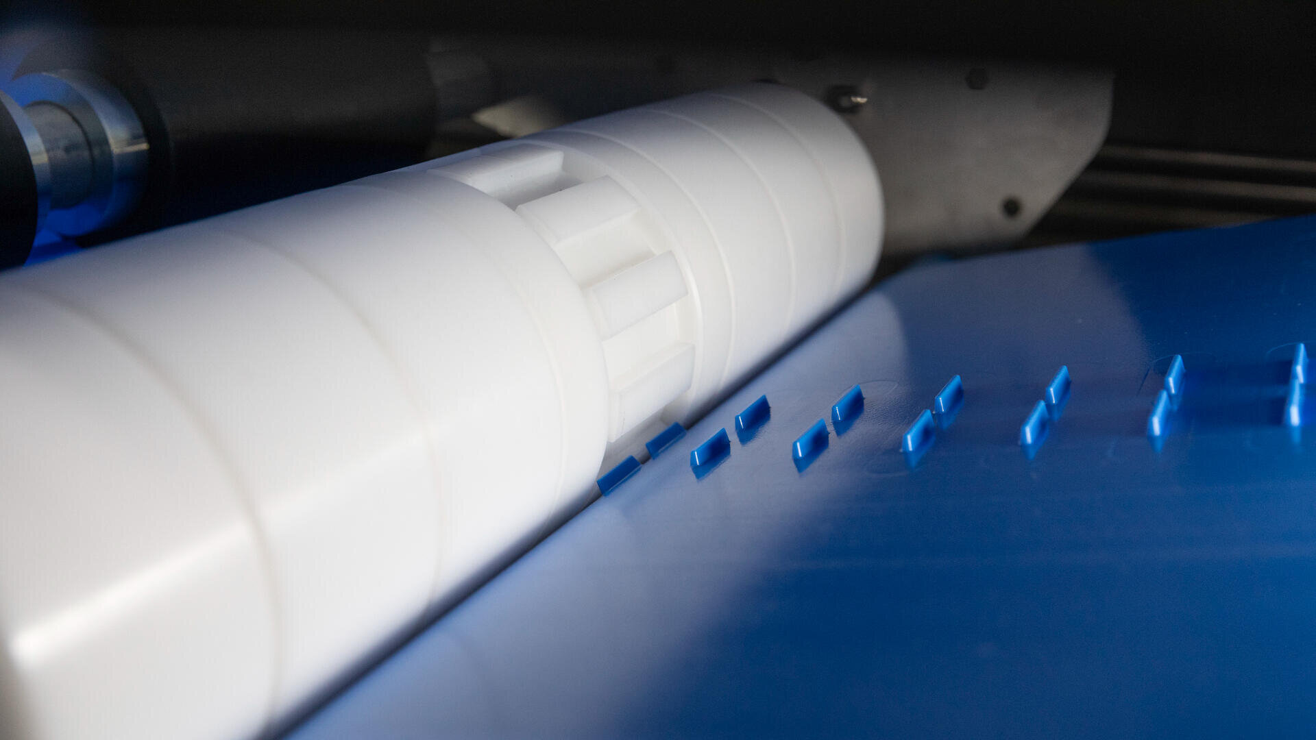 Close-up of a white industrial roller and blue plastic pieces on a blue conveyor, likely part of a manufacturing or sorting machine.
