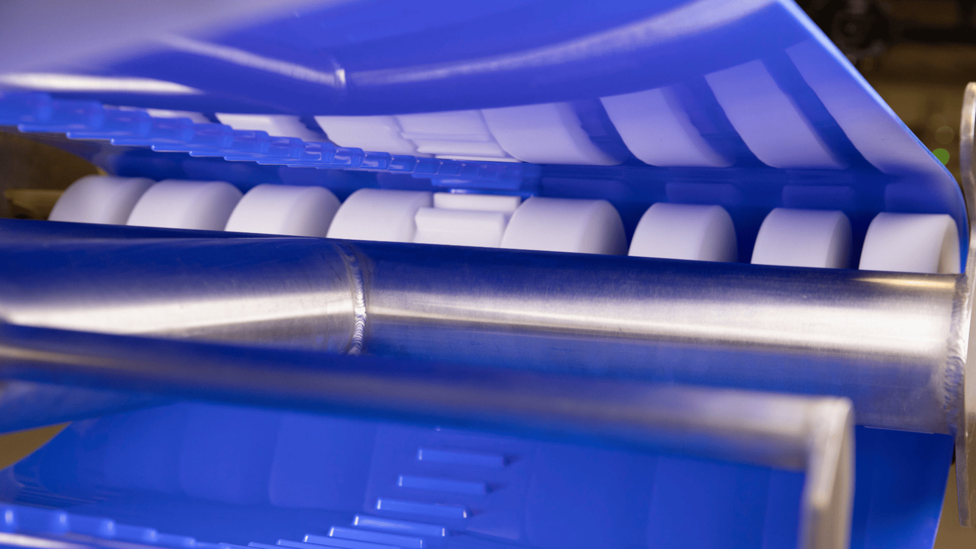 Close-up view of a modern industrial machine with blue and metallic surfaces, featuring several white cylindrical rollers and a reflective metal tube.