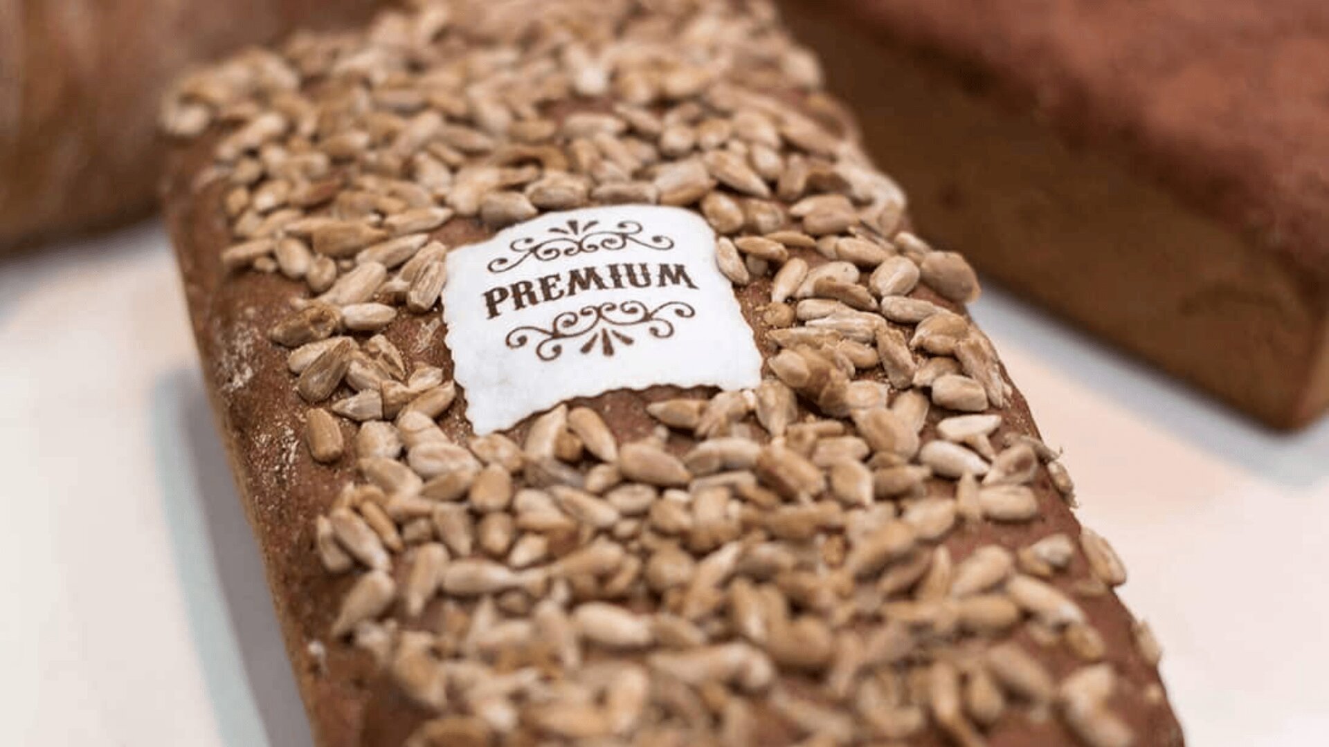 A loaf of bread topped with sunflower seeds, featuring a white label in the center that reads PREMIUM in decorative text.
