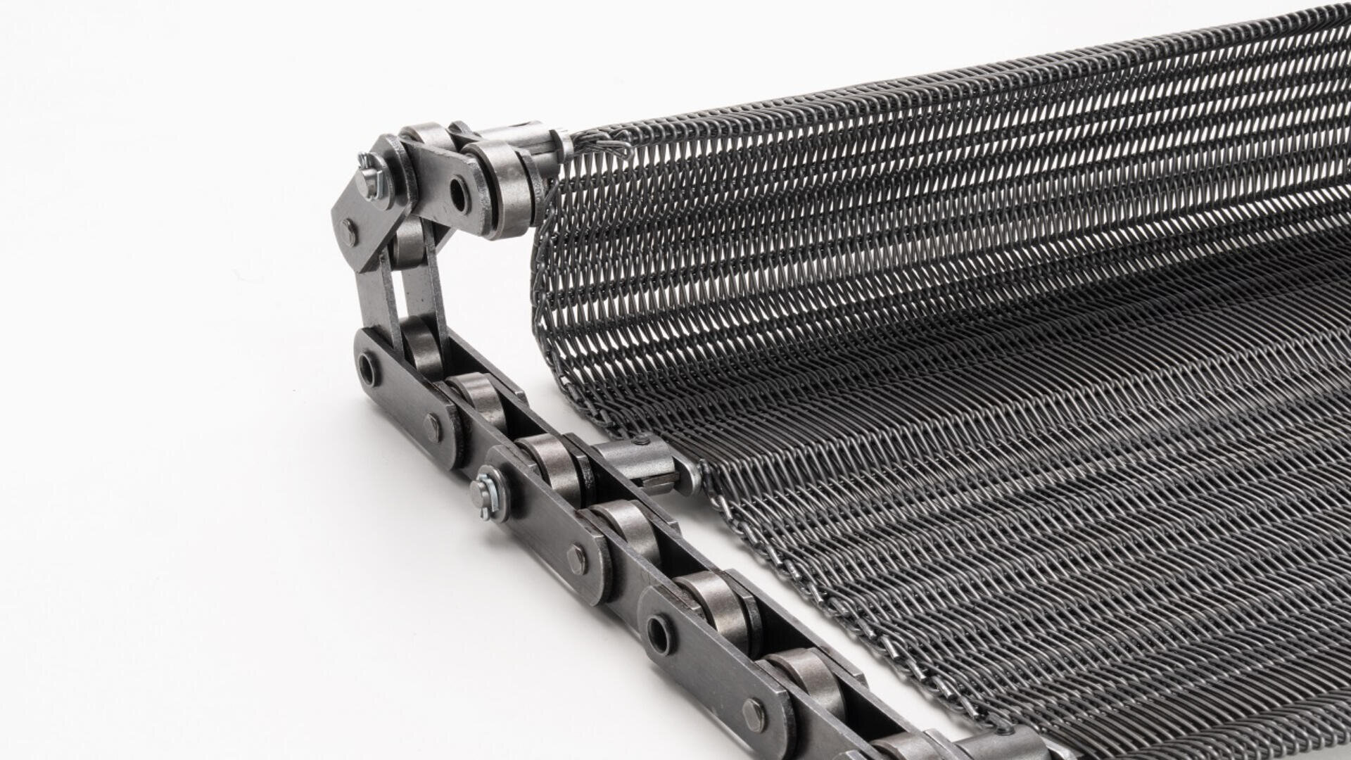 A close-up of a metal conveyor belt with interwoven wire mesh and a chain drive system, partially rolled on a white background.