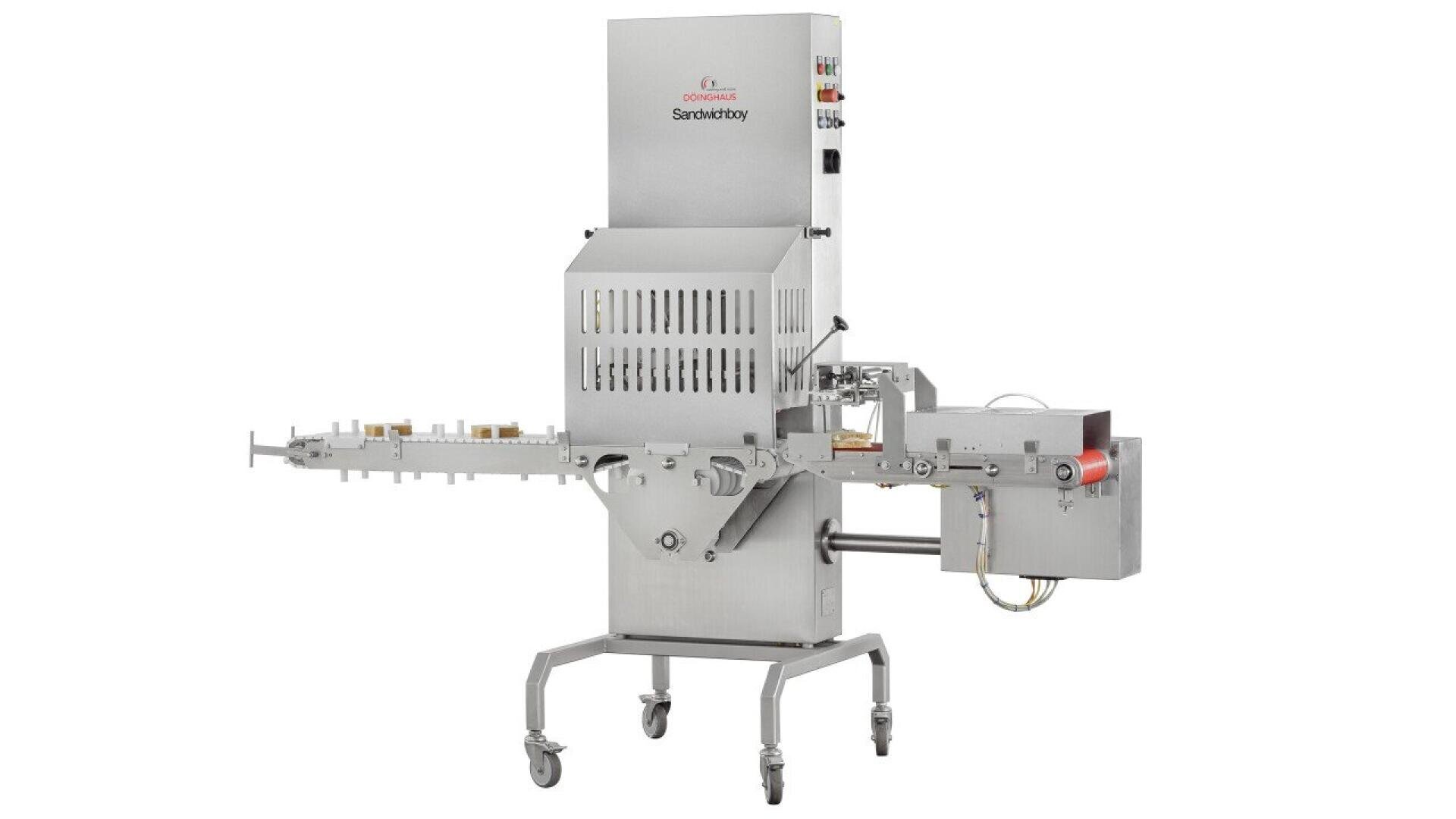 A stainless steel industrial machine with control panels, vents, and a conveyor belt on wheels, used in food processing or manufacturing, isolated on a white background.