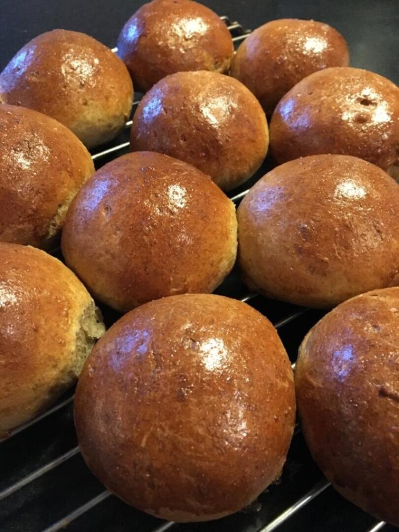 Twelve shiny, golden brown bread rolls cooling on a wire rack, with a smooth and glossy surface, arranged close together.