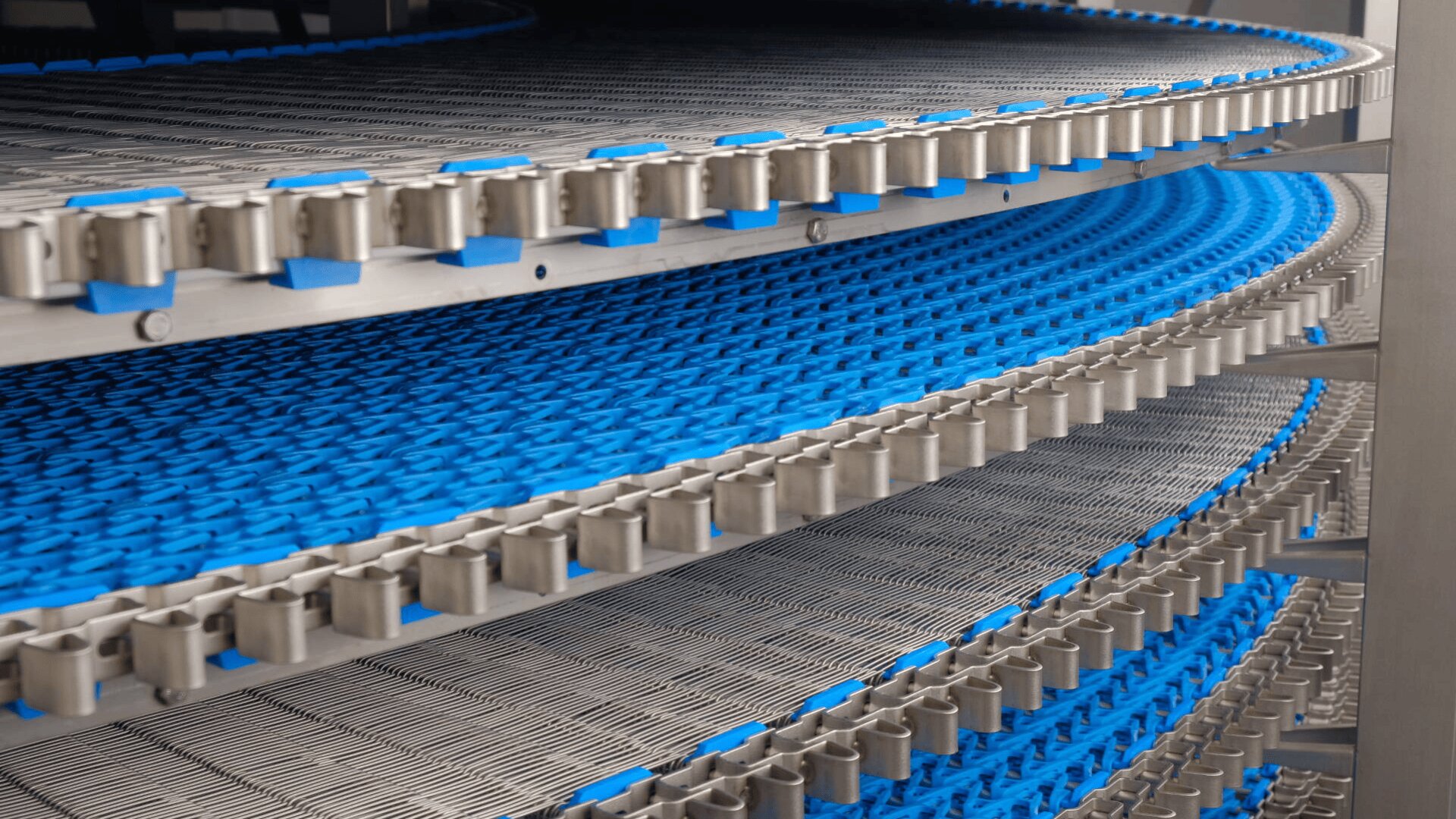 Close-up of a spiral conveyor system with blue plastic conveyor belts and metal rails winding upward in multiple layers, used for transporting goods in industrial settings.