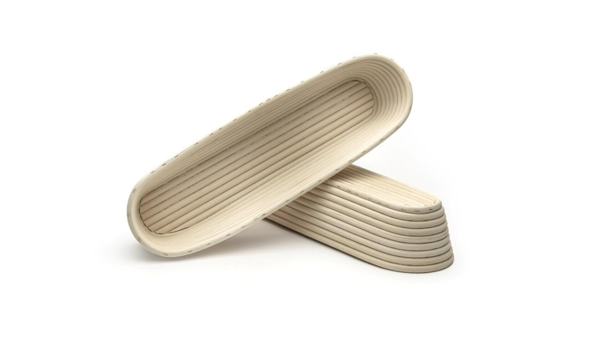 Two beige, oval-shaped, ribbed proofing baskets are stacked on a white background, with one lying flat and the other propped at an angle inside it.