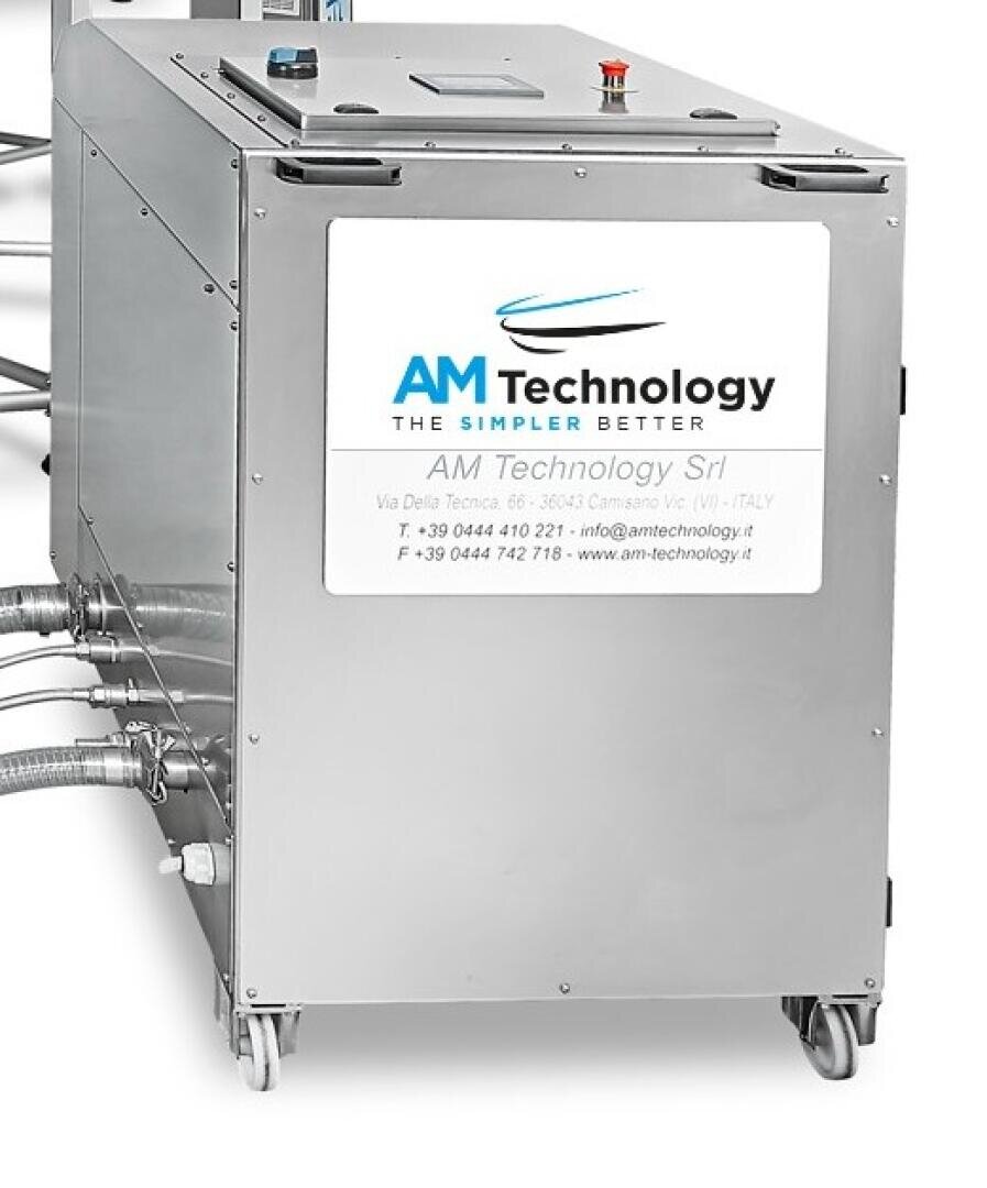 Eine Industriemaschine aus rostfreiem Stahl auf Rädern mit einem Schild mit der Aufschrift AM Technology und Kontaktinformationen des Unternehmens auf der Frontplatte. An der Seite sind mehrere Kabel und Rohre angeschlossen.
