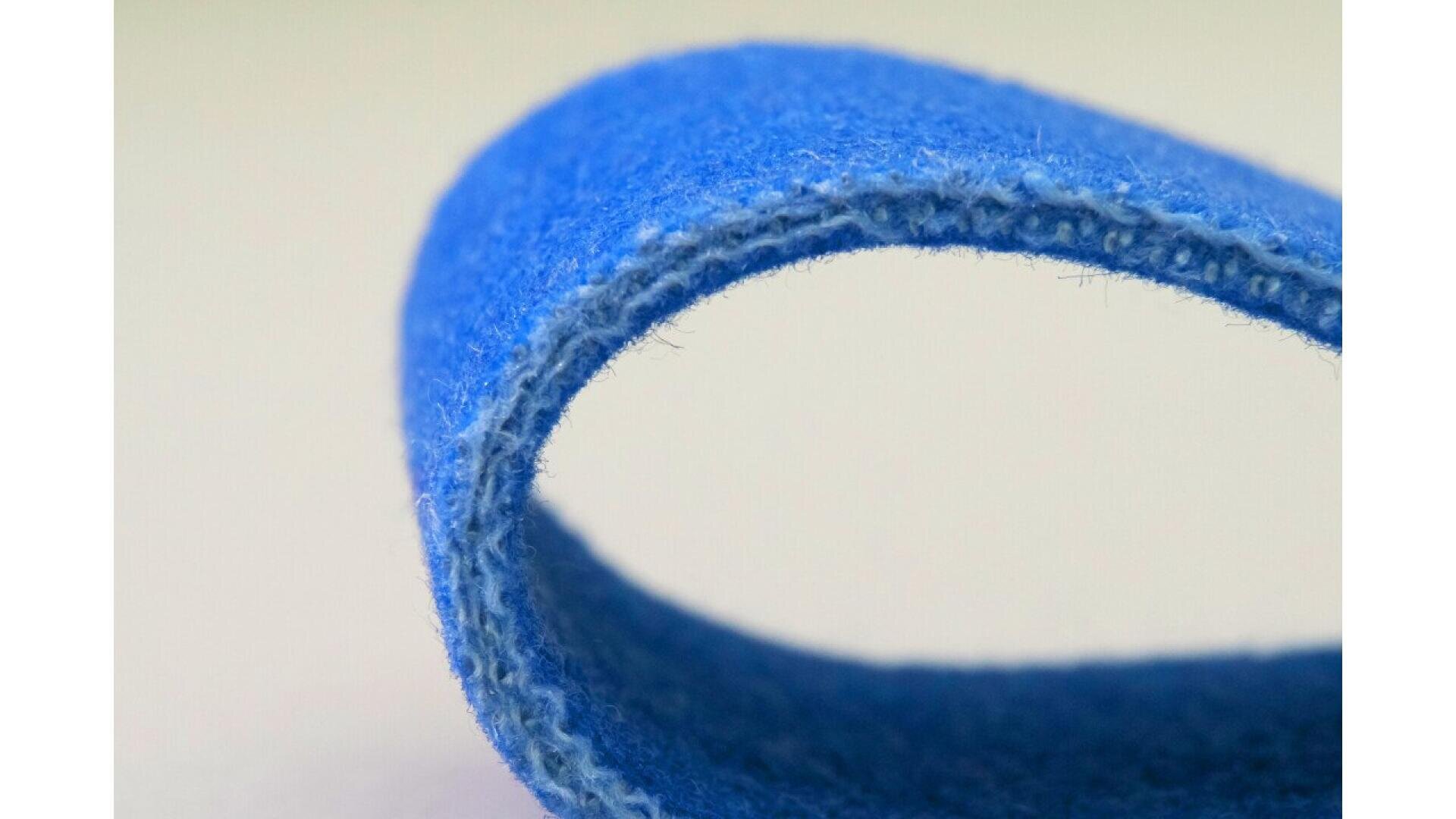 Nahaufnahme eines blauen Klettverschlussstreifens, der in einer Kurve gebogen ist und die unscharfe Textur und die Fasern im Detail vor einem einfarbigen Hintergrund zeigt.