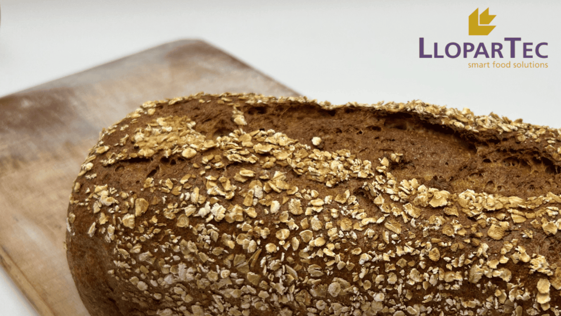Auf einem Holzbrett liegt ein Laib Vollkornbrot mit Haferflocken. In der oberen rechten Ecke sind das Logo von LloparTec und die Worte „Smart Food Solutions“ zu sehen.