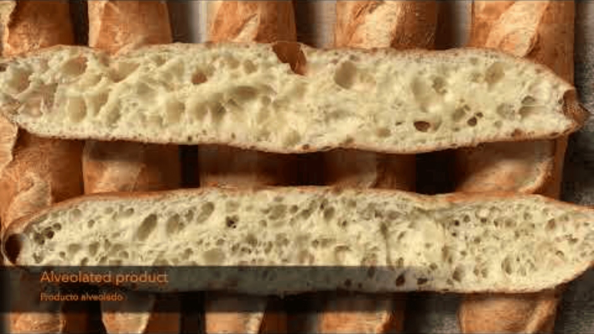 Abgebildet sind zwei Baguettescheiben mit offener, luftiger Krumenstruktur, die auf einem ganzen Baguette liegen. Der Text in der Ecke lautet "Alveoliertes Produkt" und "Producto alveolado.".