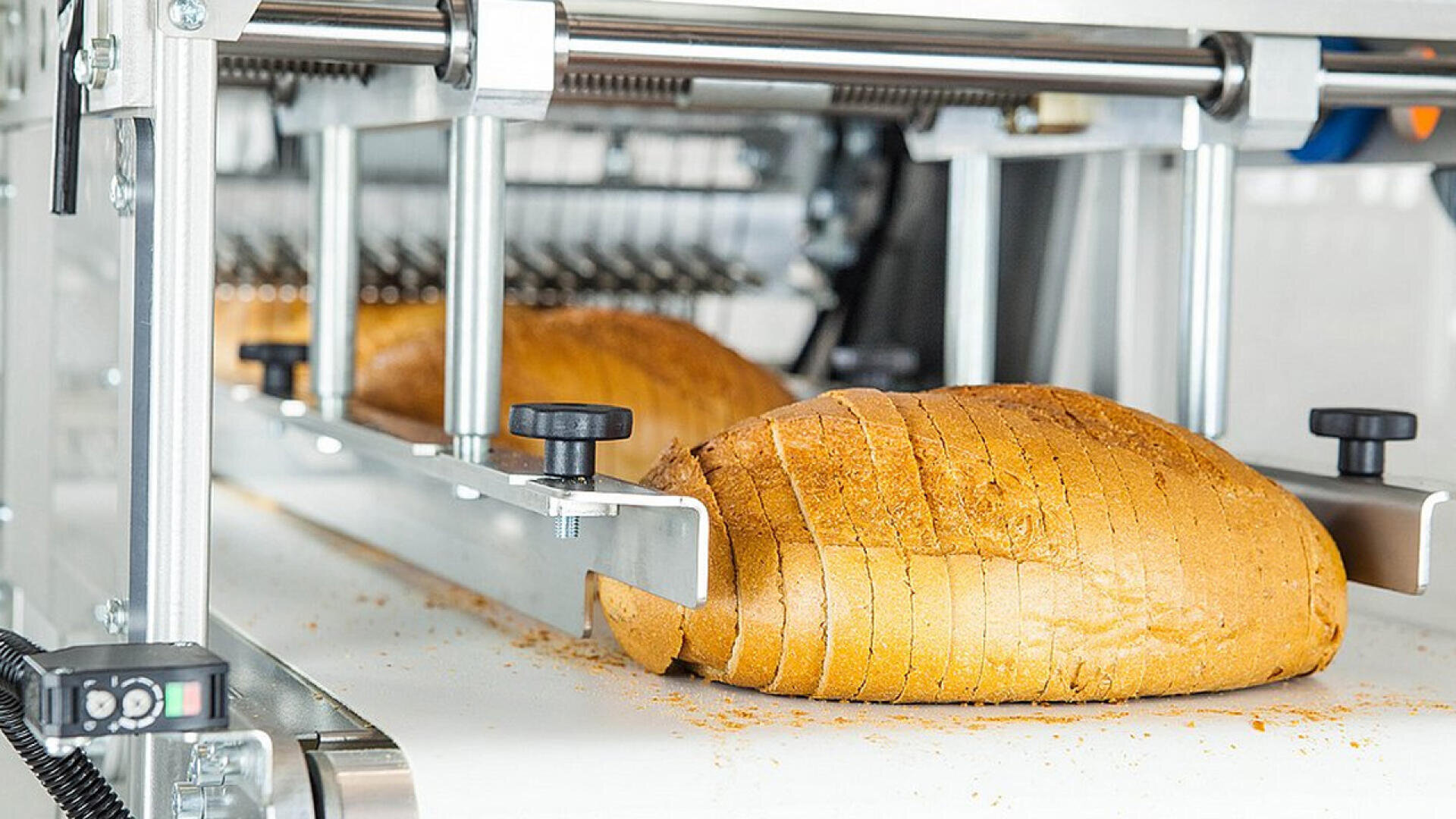 A loaf of bread being evenly sliced by an industrial bread slicing machine in a bakery setting.