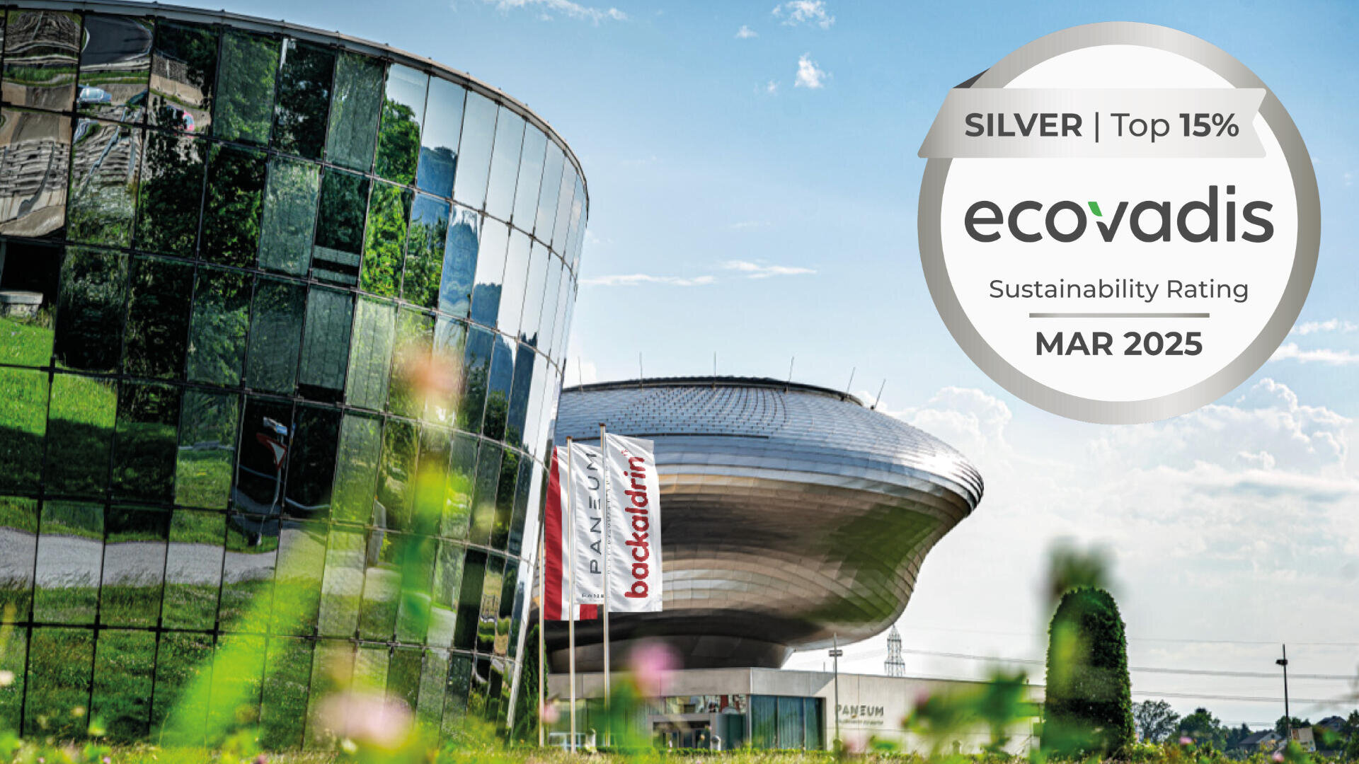 A modern glass building and a futuristic structure with flags in front. Overlay: SILVER | Top 15% ecovadis Sustainability Rating MAR 2025.