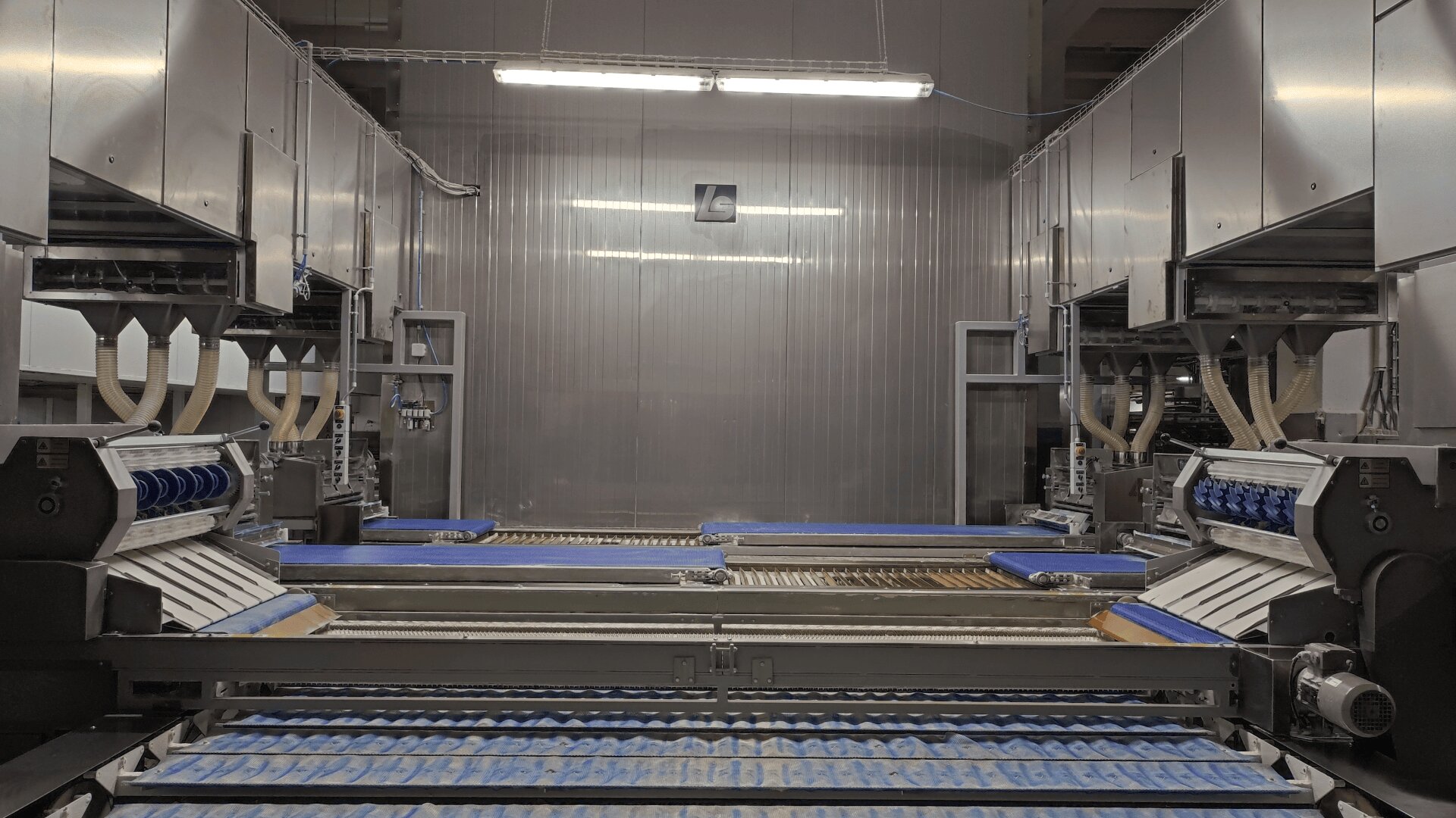 A modern industrial bakery production line with automated machines and conveyor belts, featuring rollers and trays for processing baked goods in a clean, well-lit facility.
