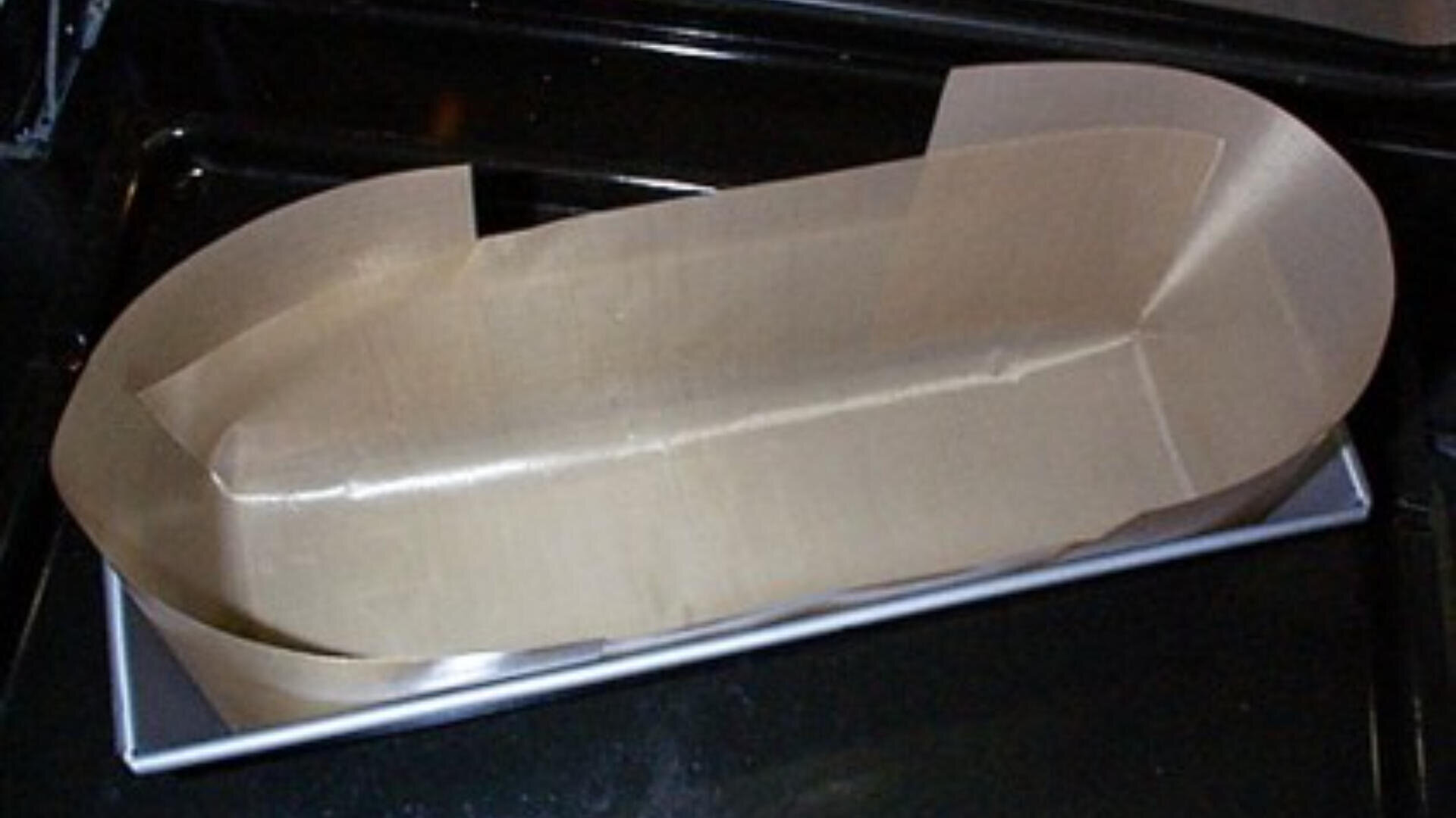 Eine mit braunem Pergamentpapier ausgelegte Laibform, die an den Seiten und am Boden sauber eingepasst ist, steht auf einem Ofenrost.