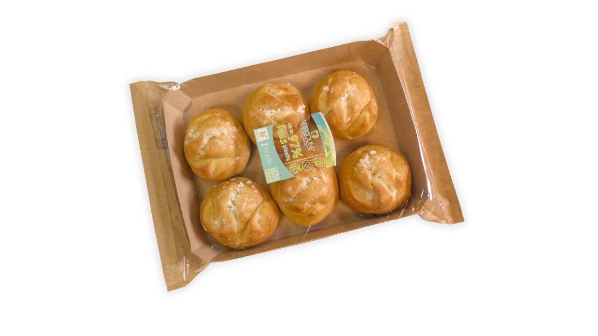 Ein braunes Papptablett mit sechs runden Brötchen, teilweise in durchsichtiges Plastik eingewickelt, mit einem kleinen Etikett auf der Oberseite, das Text und QR-Codes enthält.