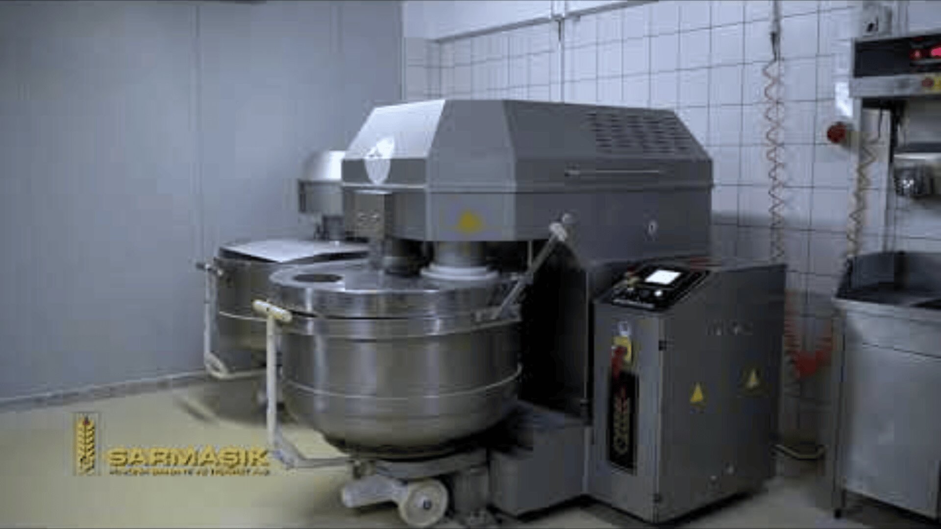 Large industrial dough mixer with a stainless steel bowl and control panel in a tiled commercial kitchen. The brand Sarmasik is visible on the image.