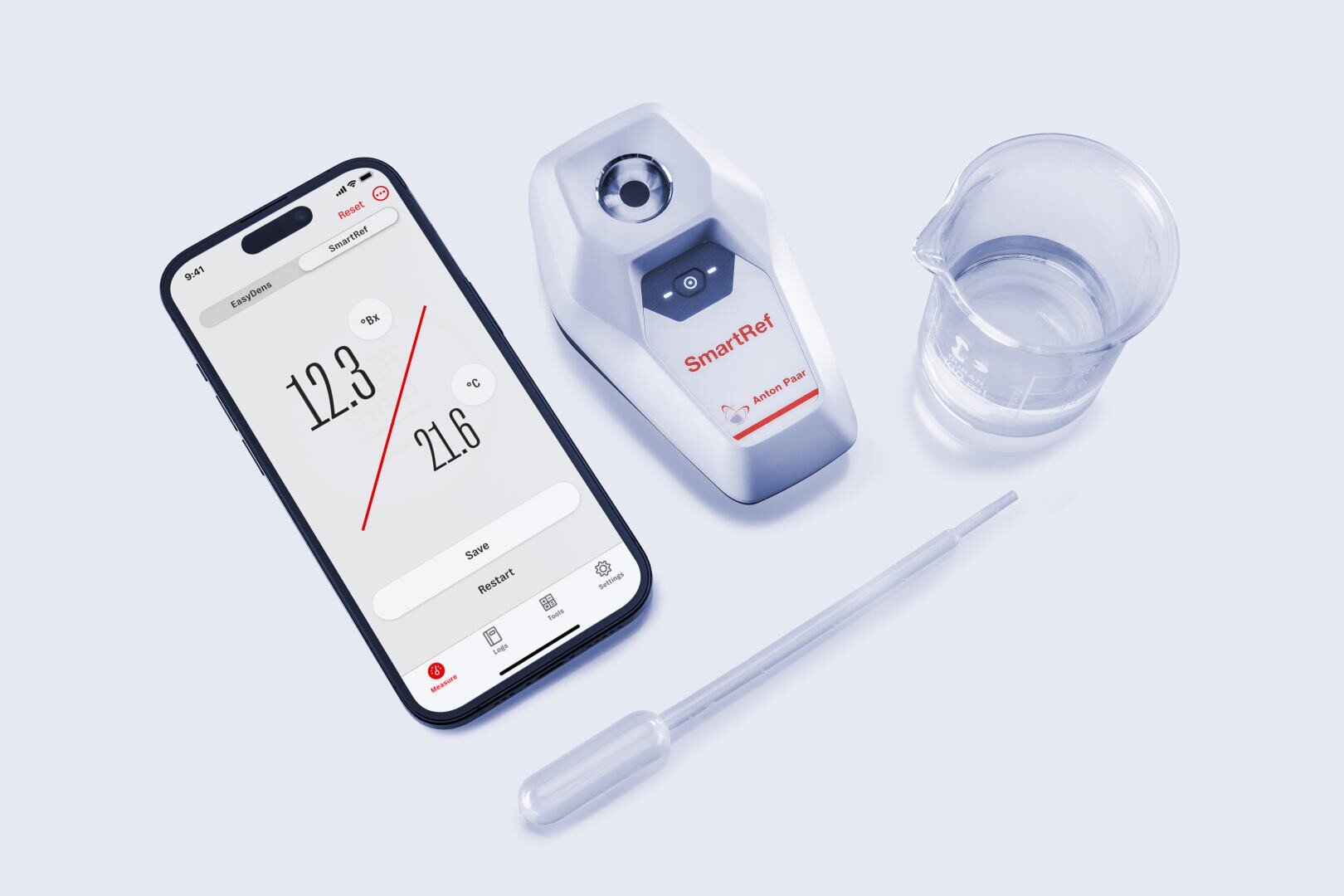 Ein Smartphone, das Messdaten anzeigt, ein digitales SmartRef-Refraktometer, eine durchsichtige Kunststoffpipette und ein kleiner Glasbecher mit Flüssigkeit sind auf einer weißen Fläche angeordnet.