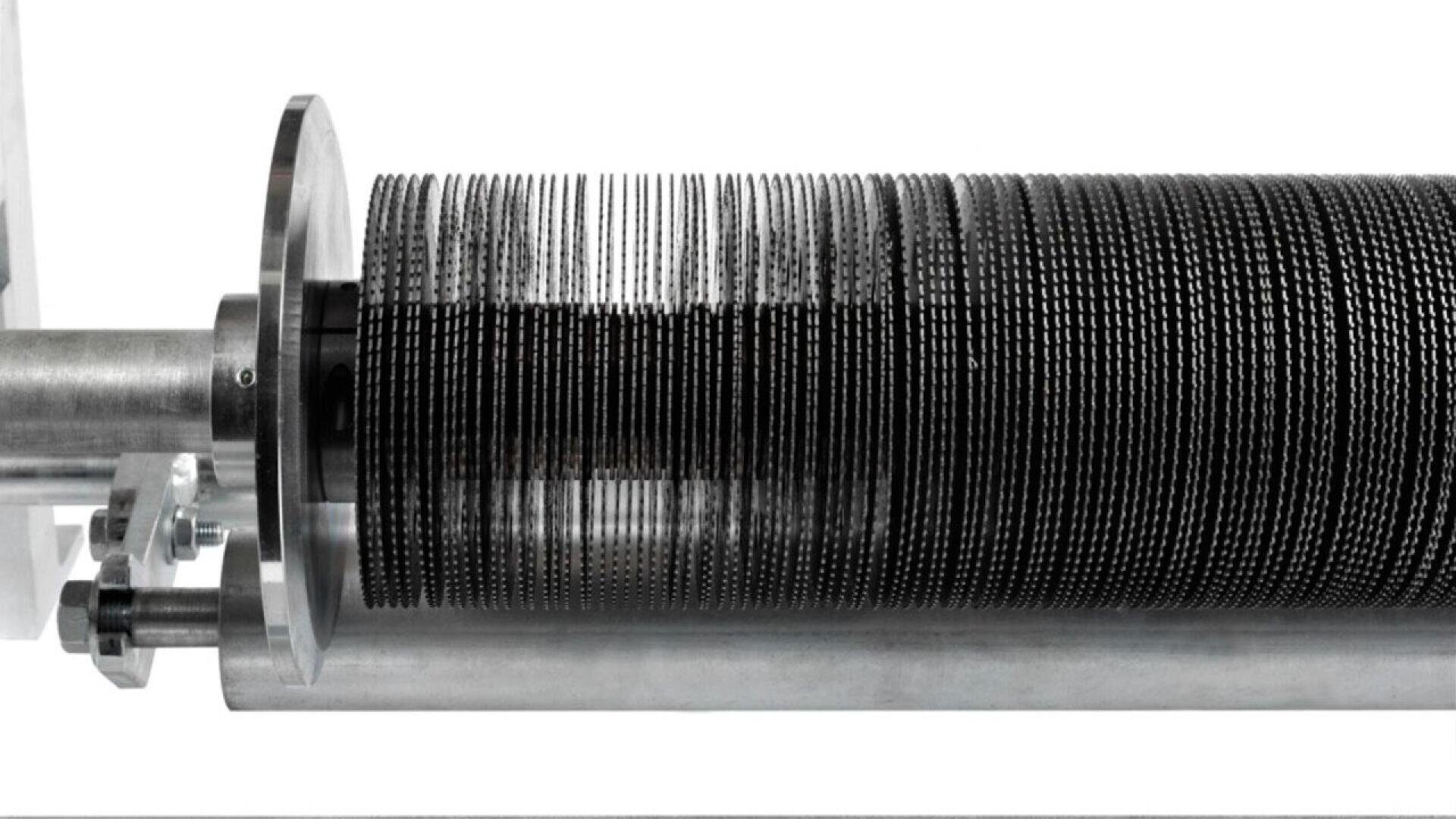 A close-up of a cylindrical industrial machine part with many thin, evenly spaced metal discs stacked along its axis, mounted on a horizontal metal rod against a white background.