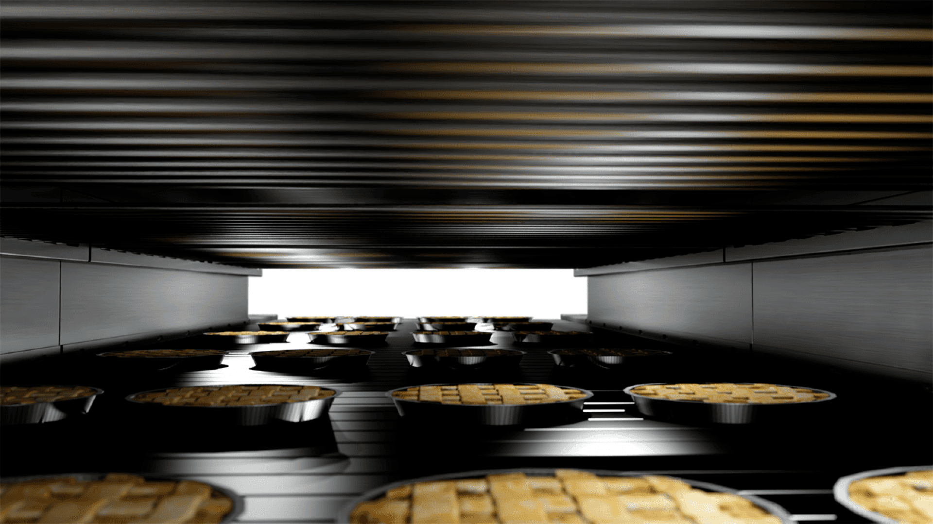 Nahaufnahme eines gewerblichen Backofens, der Reihen von kleinen Kuchen mit Gitterkruste zeigt, die auf einem Förderband unter Metallheizkörpern gebacken werden.