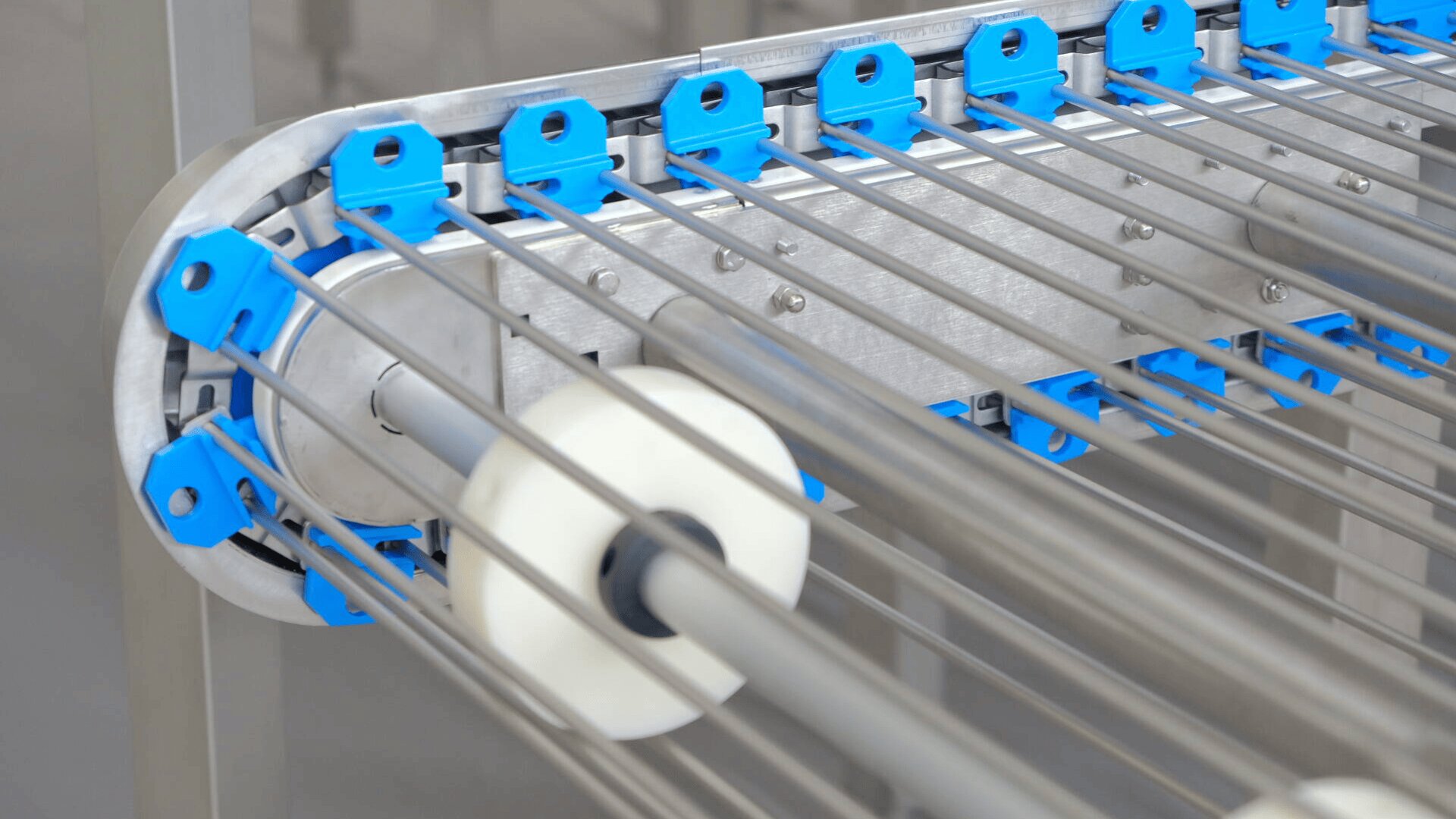 Close-up of an industrial machine with multiple parallel metal rods, blue plastic holders, and two white cylindrical rollers, likely used for processing or transporting materials.