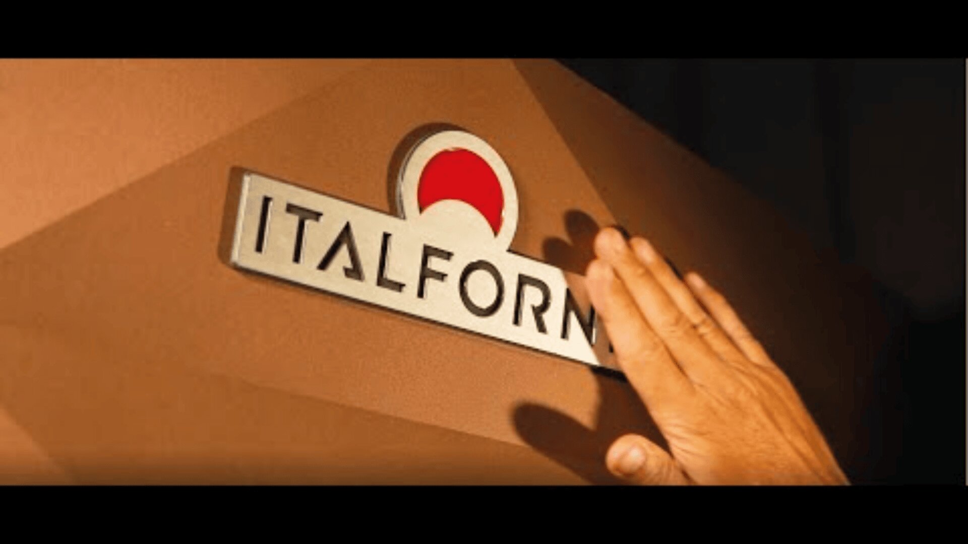 A hand touches a sign on a brown wall that reads ITALFORM with a red and white circular logo above the text.