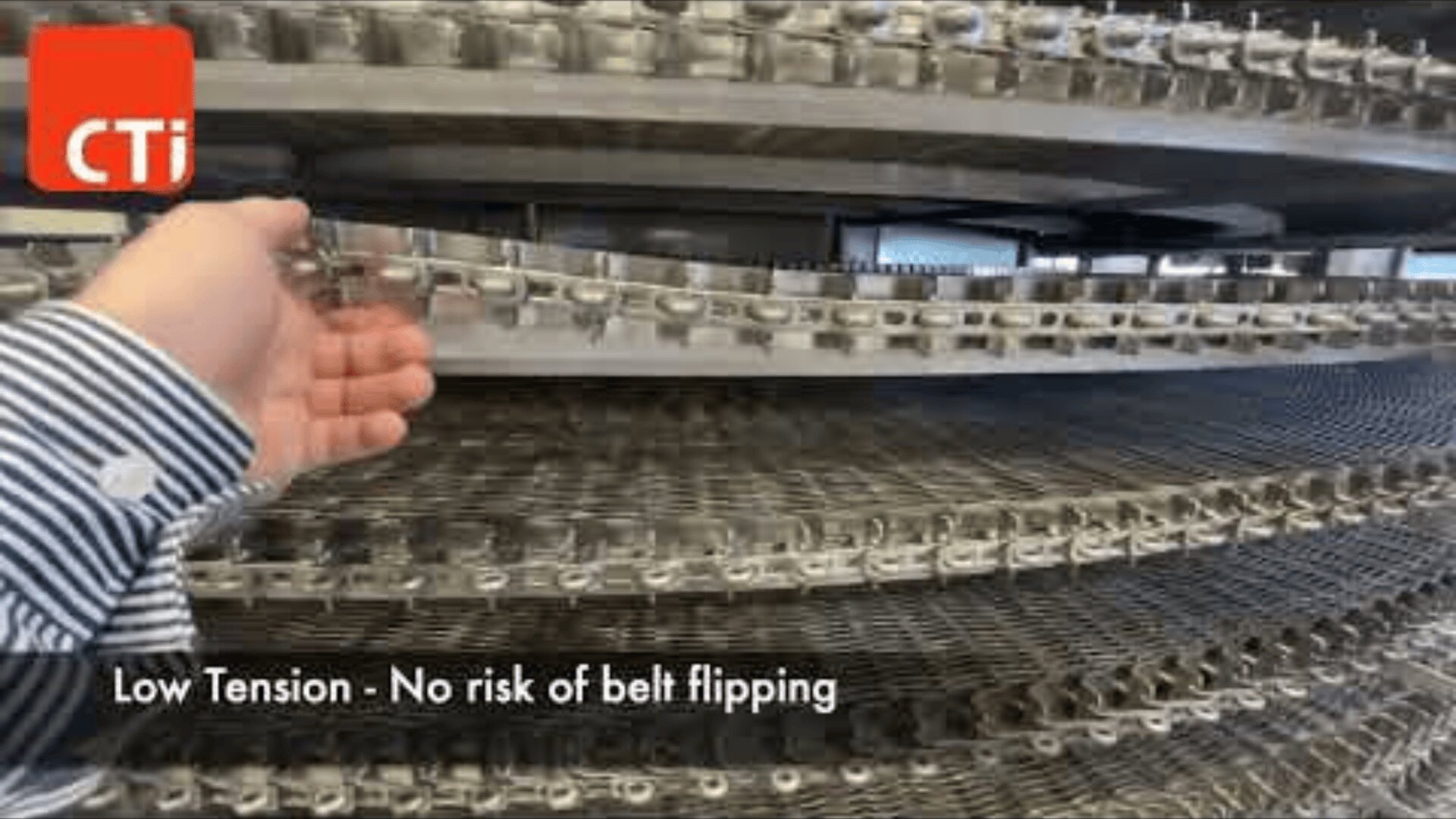 A hand checks a metal conveyor belt system with multiple spiral levels. The text reads: Low tension – no risk of belt tipping. A red CTi logo appears in the upper left corner.