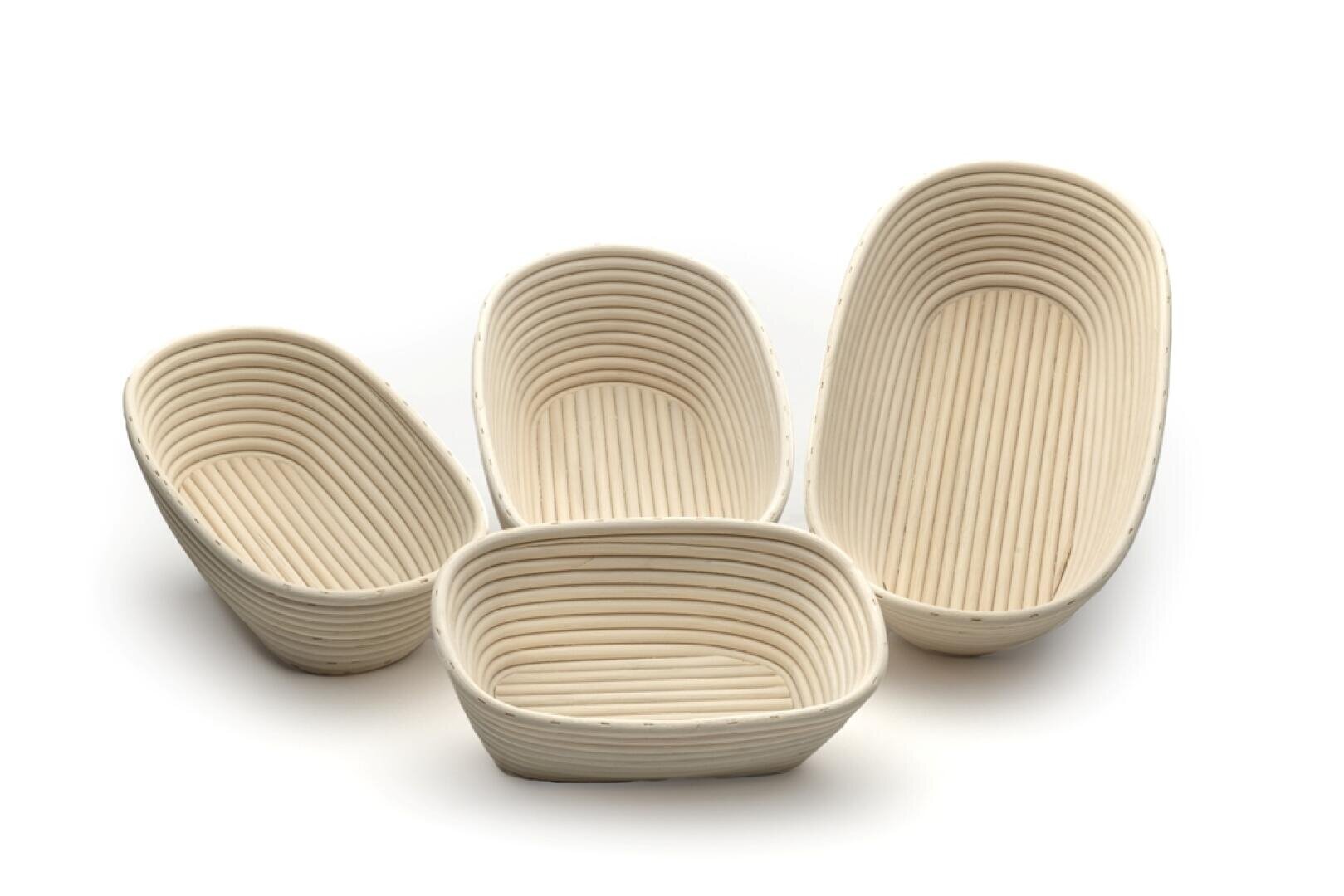 Vier leere, cremefarbene, ovale und rechteckige Brotgärkörbe (Bannetons) sind auf einer weißen Fläche angeordnet. Die Körbe haben innen eine gerippte, spiralförmige Struktur.
