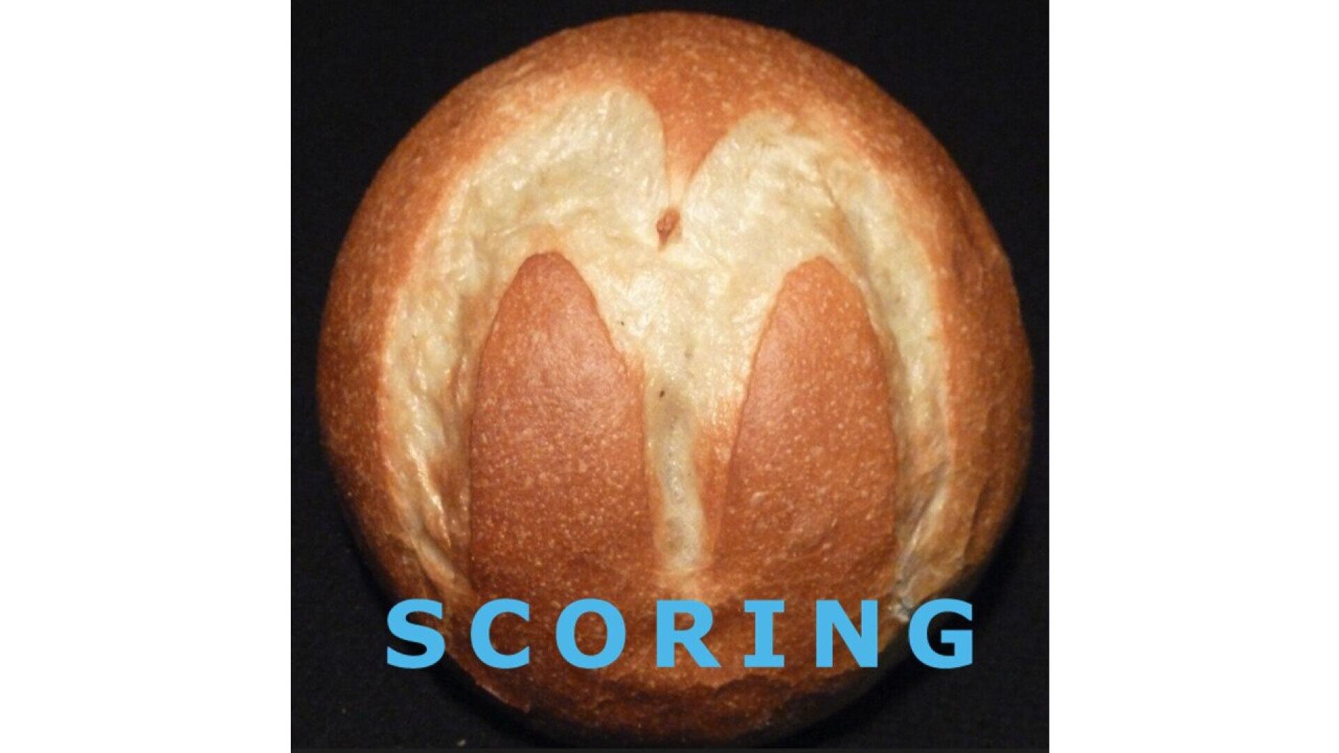 Ein rundes Brötchen mit einem eingeritzten M auf der Oberseite auf schwarzem Hintergrund. Unter dem Brötchen ist in fetten blauen Buchstaben das Wort SCORING zu lesen.