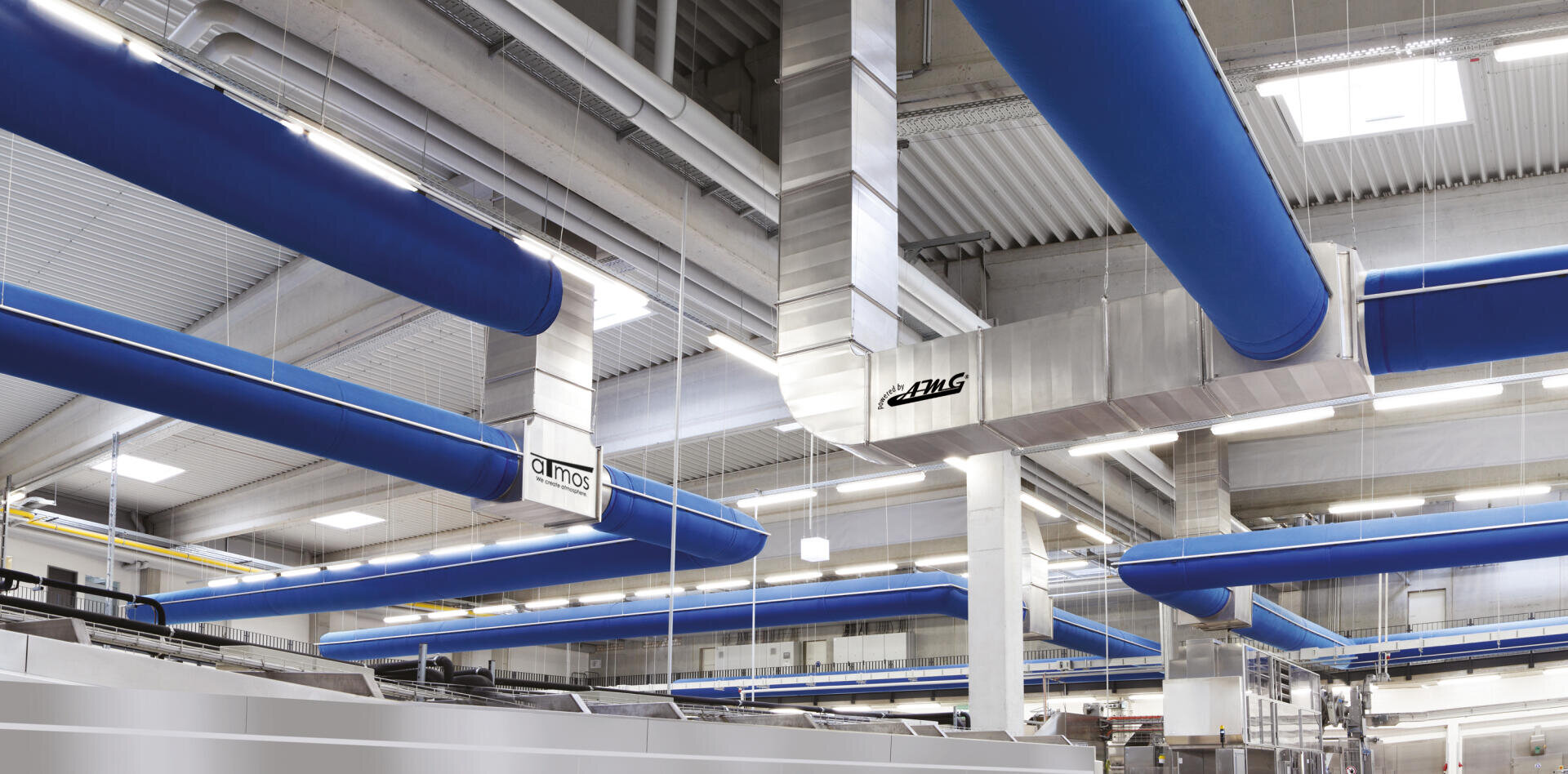 Modern industrial facility interior with large blue ventilation ducts running along the ceiling, metallic equipment, and bright lighting, creating a clean and organized environment.