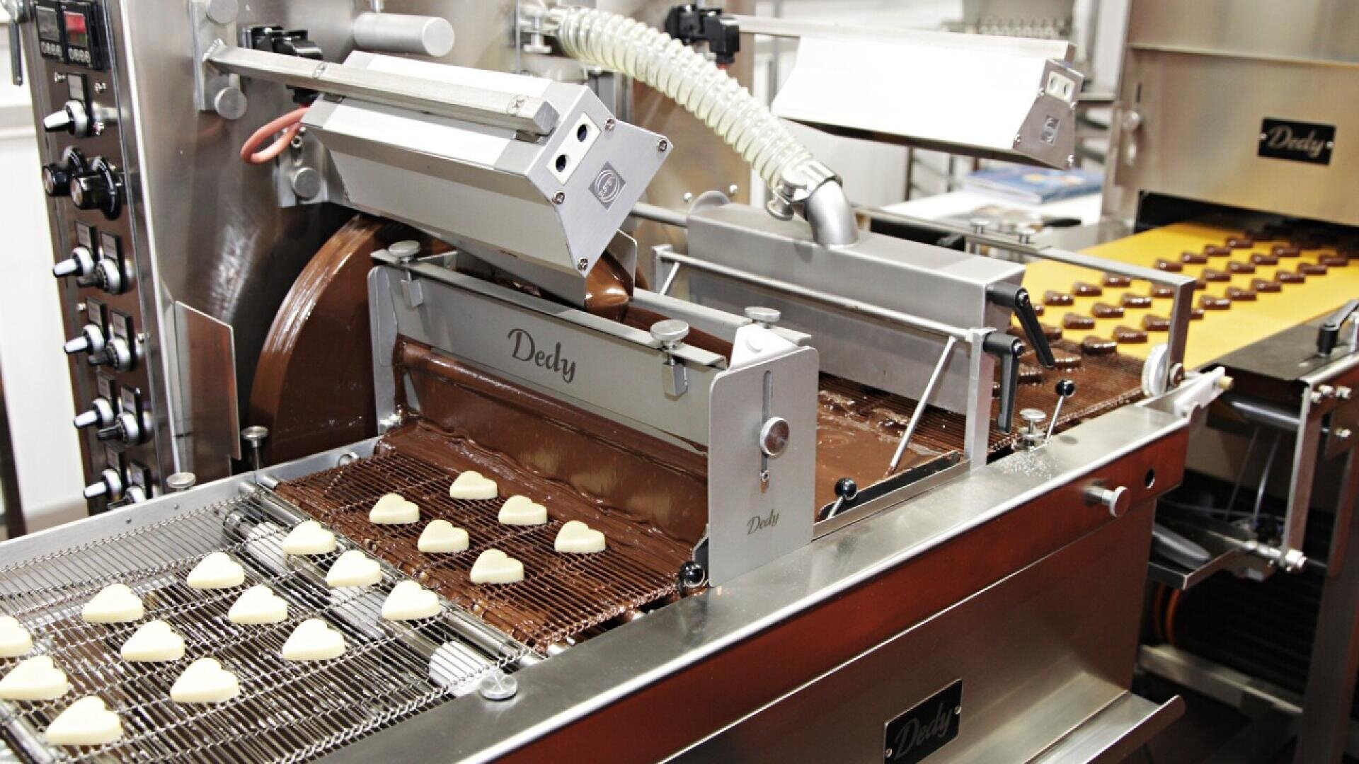 A chocolate production machine forms heart-shaped candies, moving them along a conveyor belt for coating and cooling in a modern factory setting.
